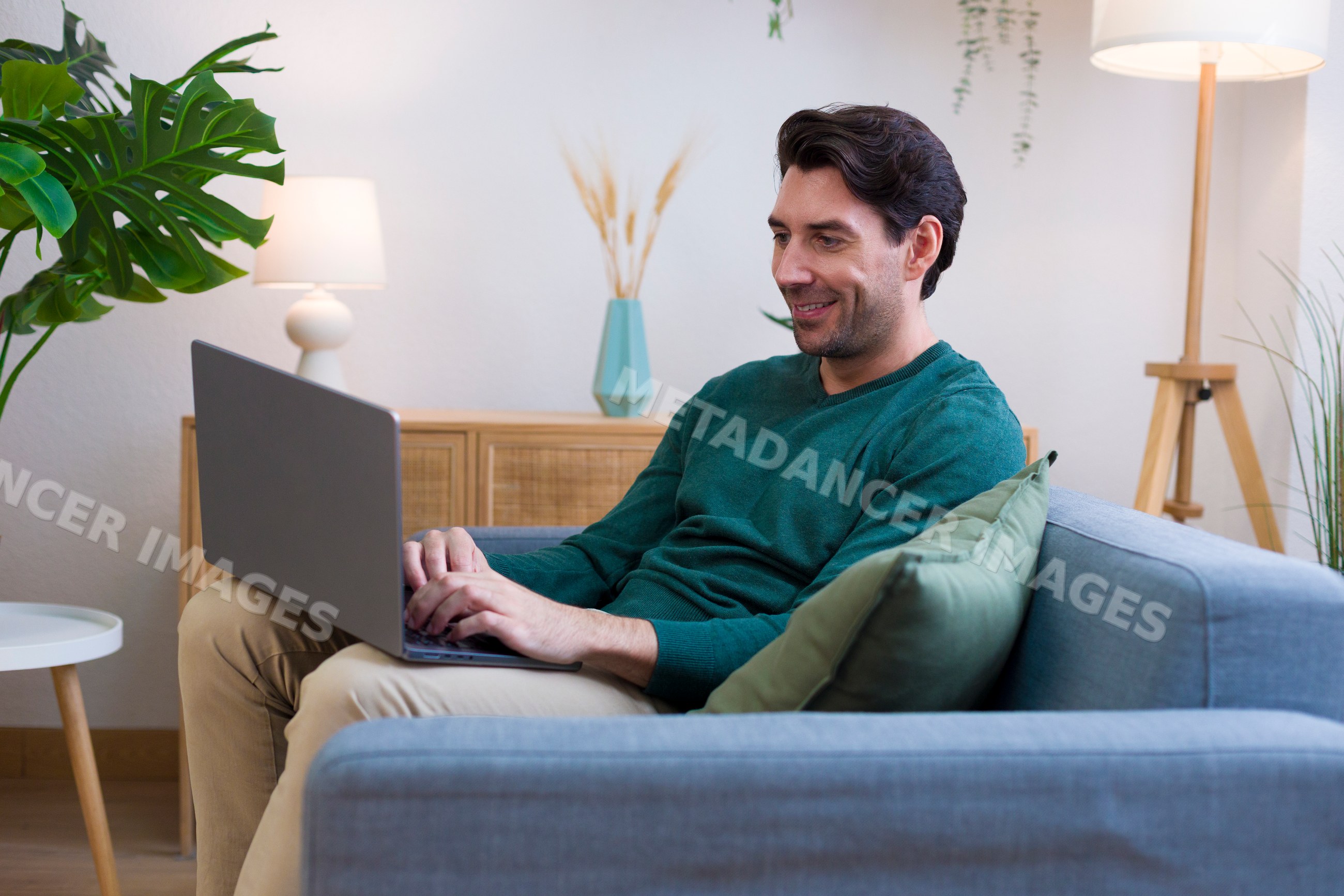 White man using laptop sitting on sofa in modern living room