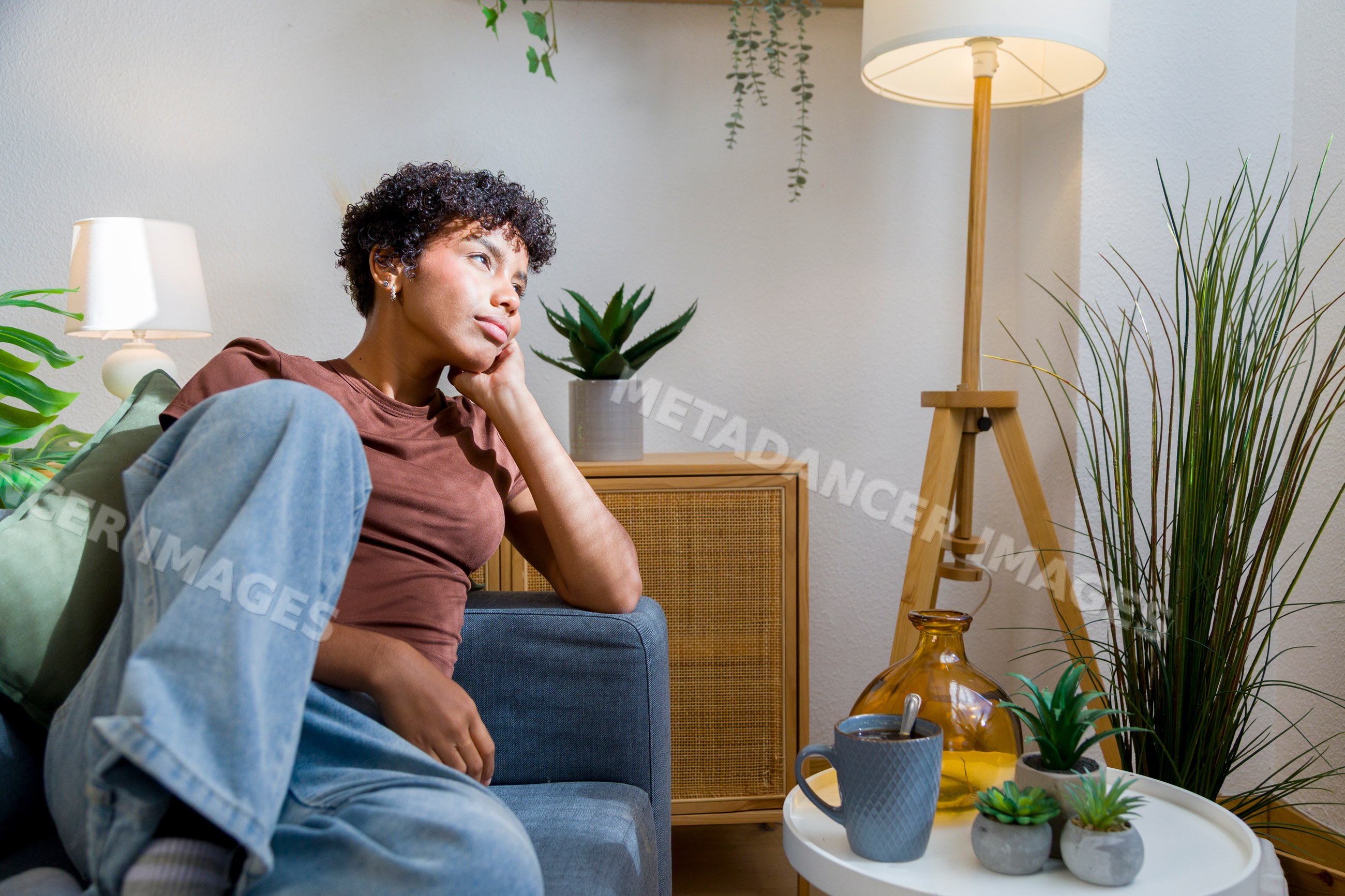 Young African American woman sitting thoughtfully on sofa
