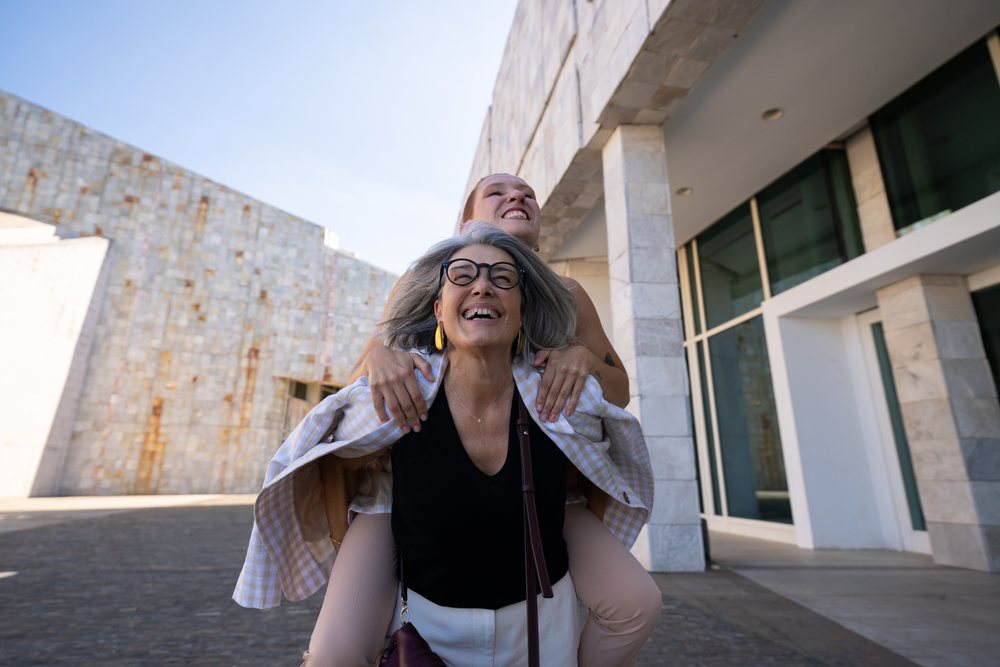 Two white women laughing and having fun with piggyback ride outside