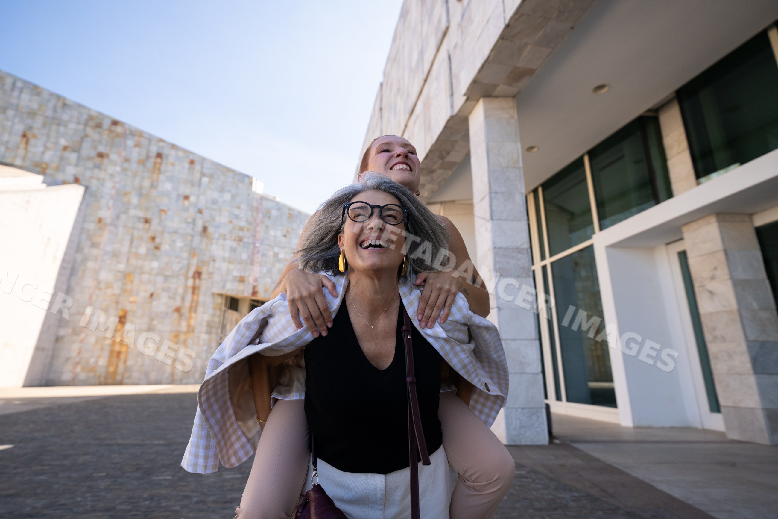Two white women laughing and having fun with piggyback ride outside