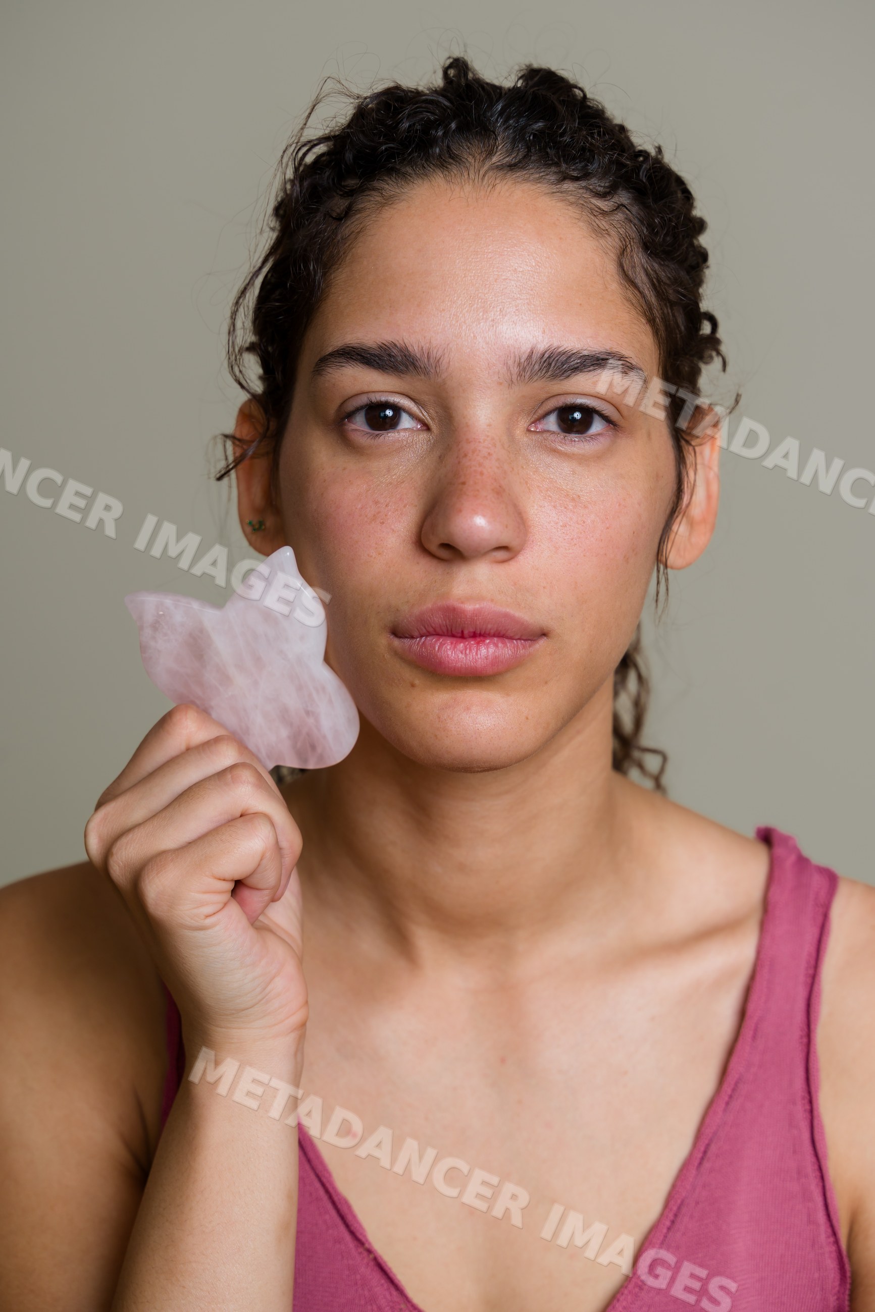 Hispanic woman using rose quartz gua sha facial massage tool