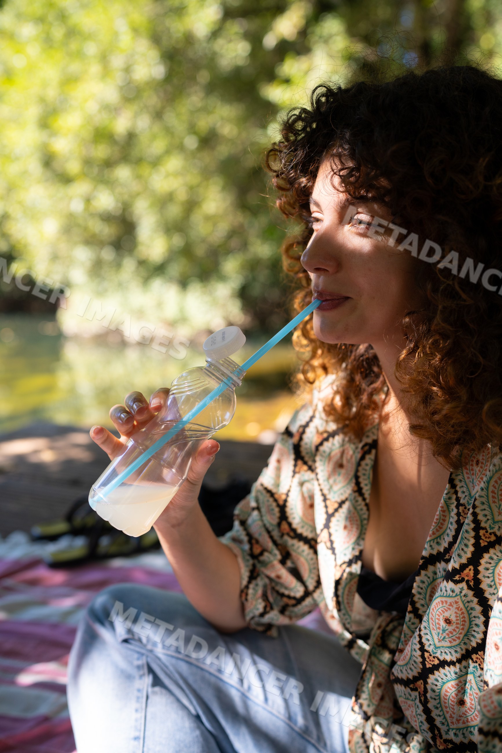 White woman drinking from plastic bottle outdoors on picnic blanket