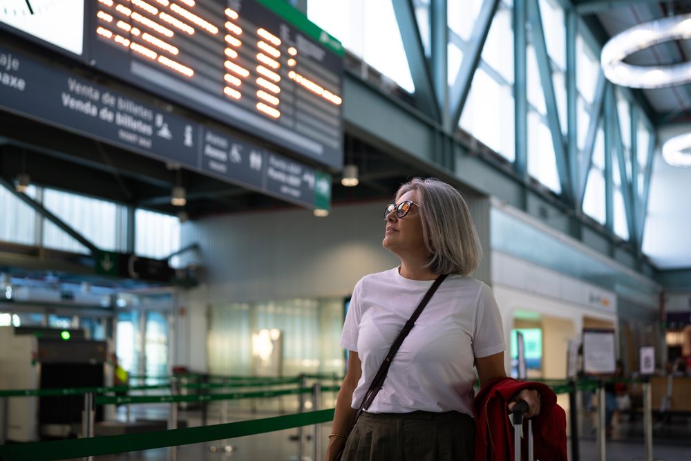 White woman waiting at airport departure ticket counter with luggage