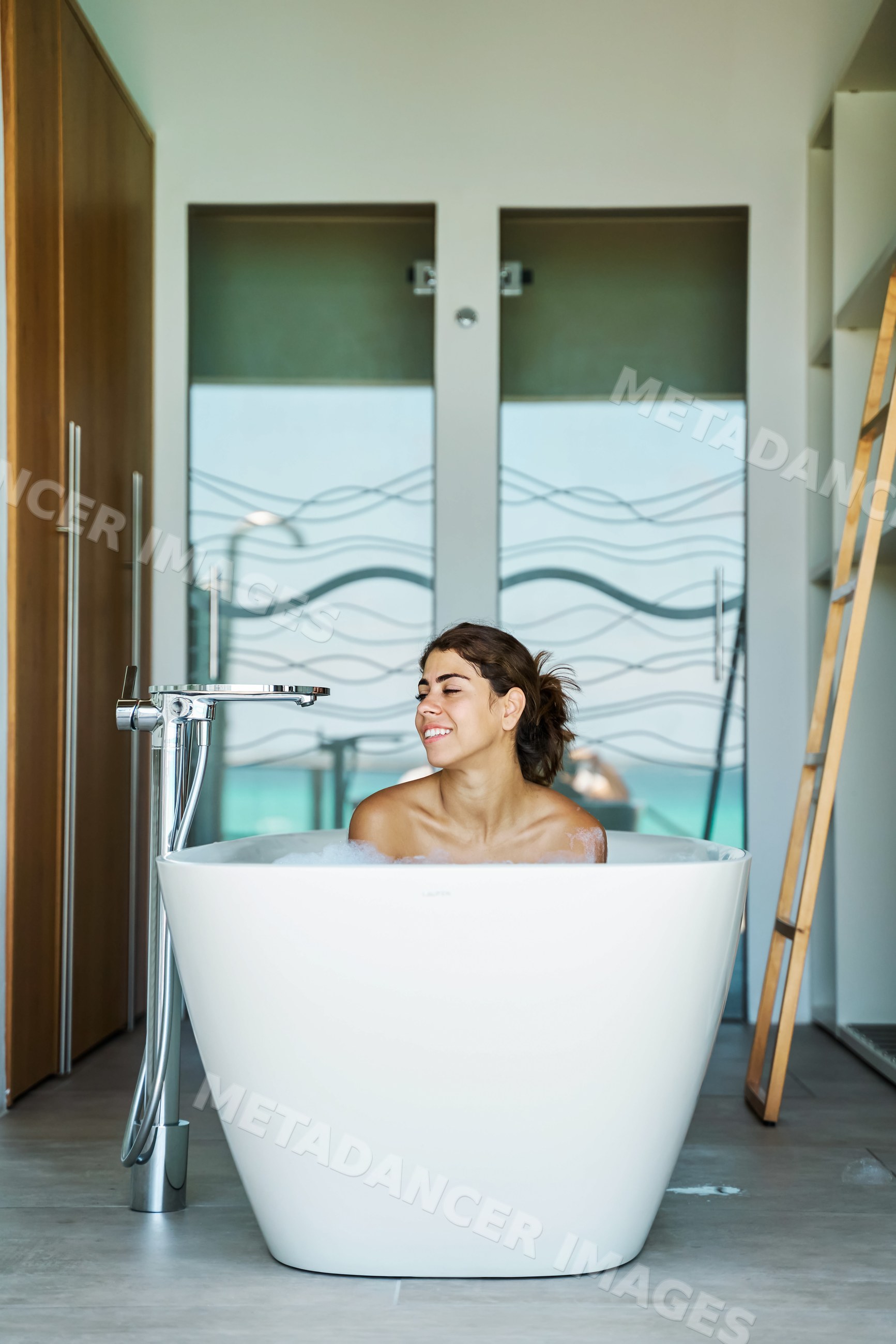 A white woman relaxes in a bubble bath inside a modern bathroom