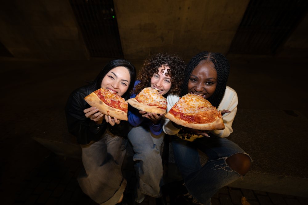 Three Hispanic, white and Black women eating pepperoni and cheese