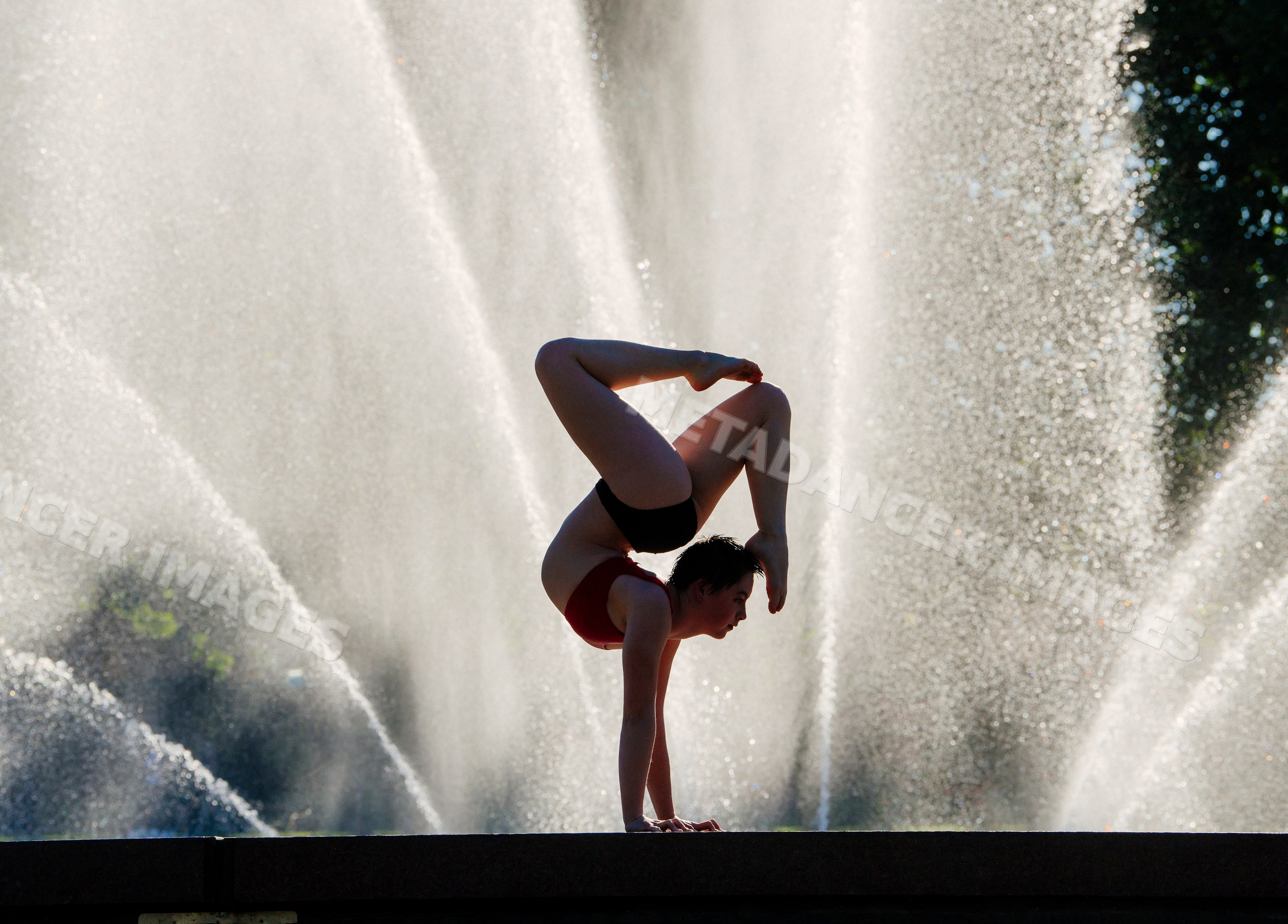 White woman performing flexible handstand pose by fountain outdoors