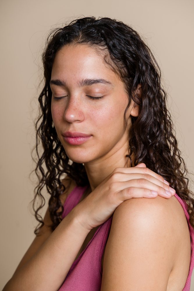 Hispanic woman with curly hair relaxing with hand on shoulder