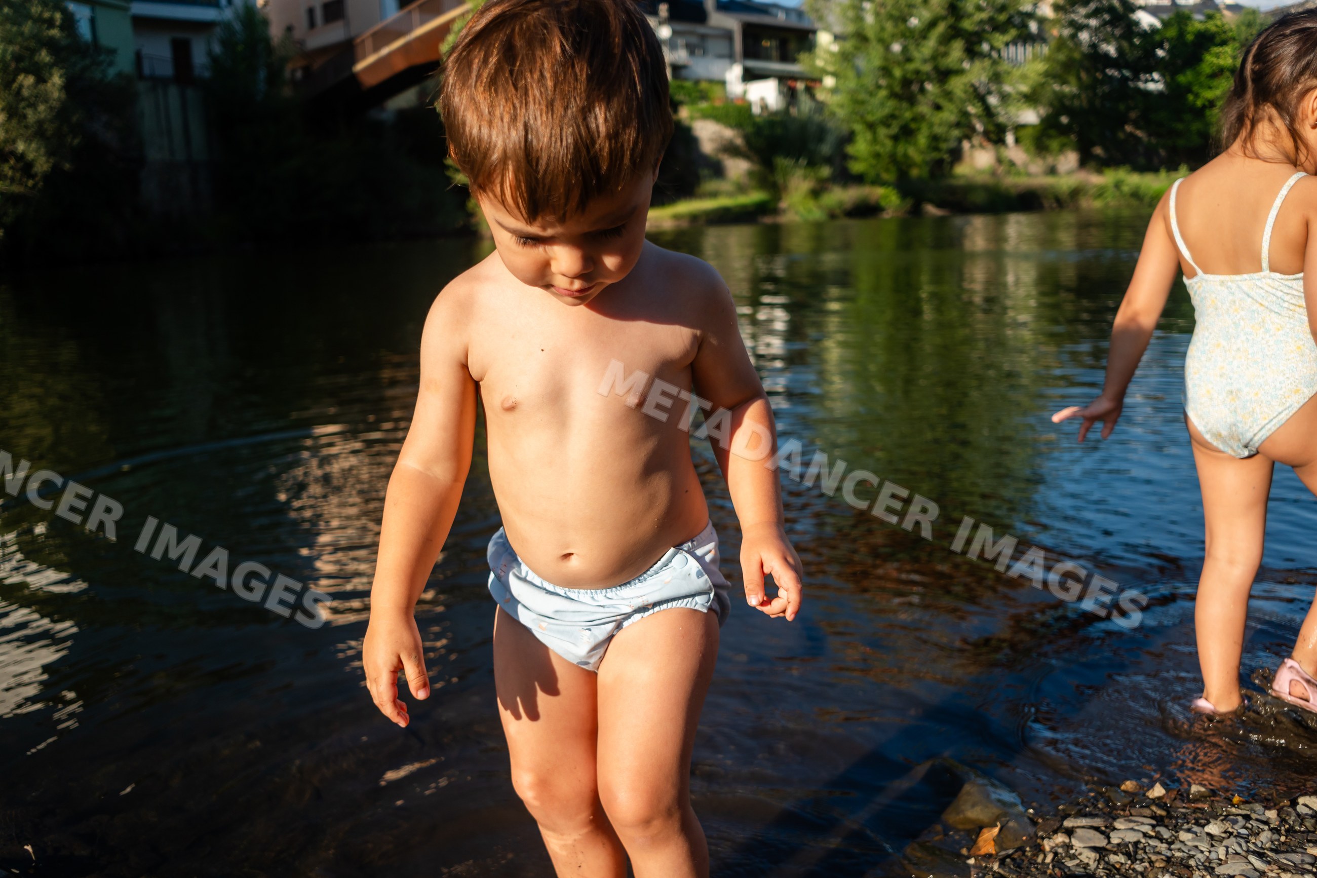 A toddler white boy wading in a shallow river on a sunny summer day