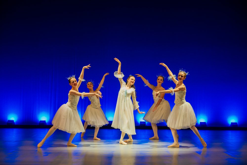 Young ballet dancers perform gracefully on stage in white costumes