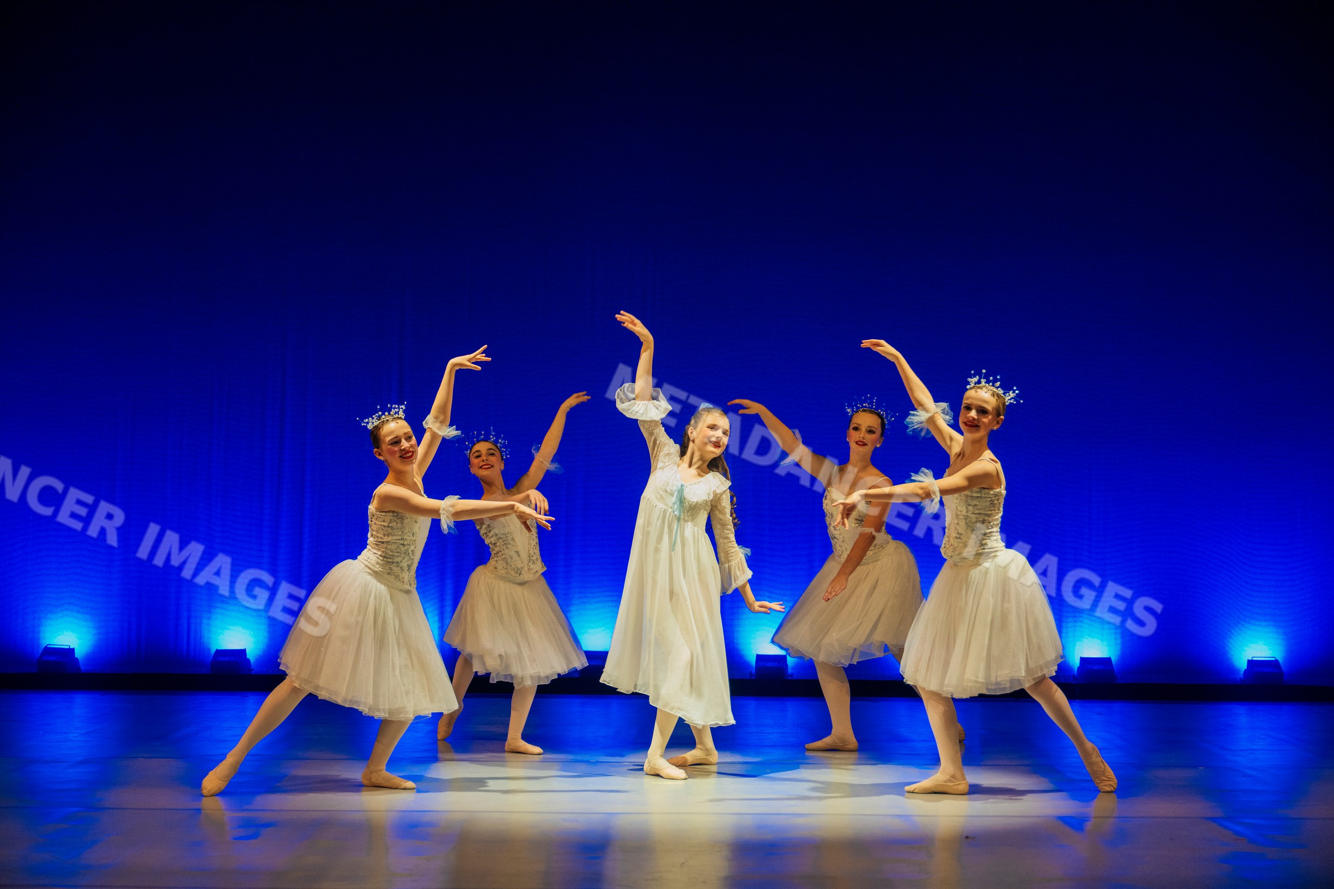 Young ballet dancers perform gracefully on stage in white costumes
