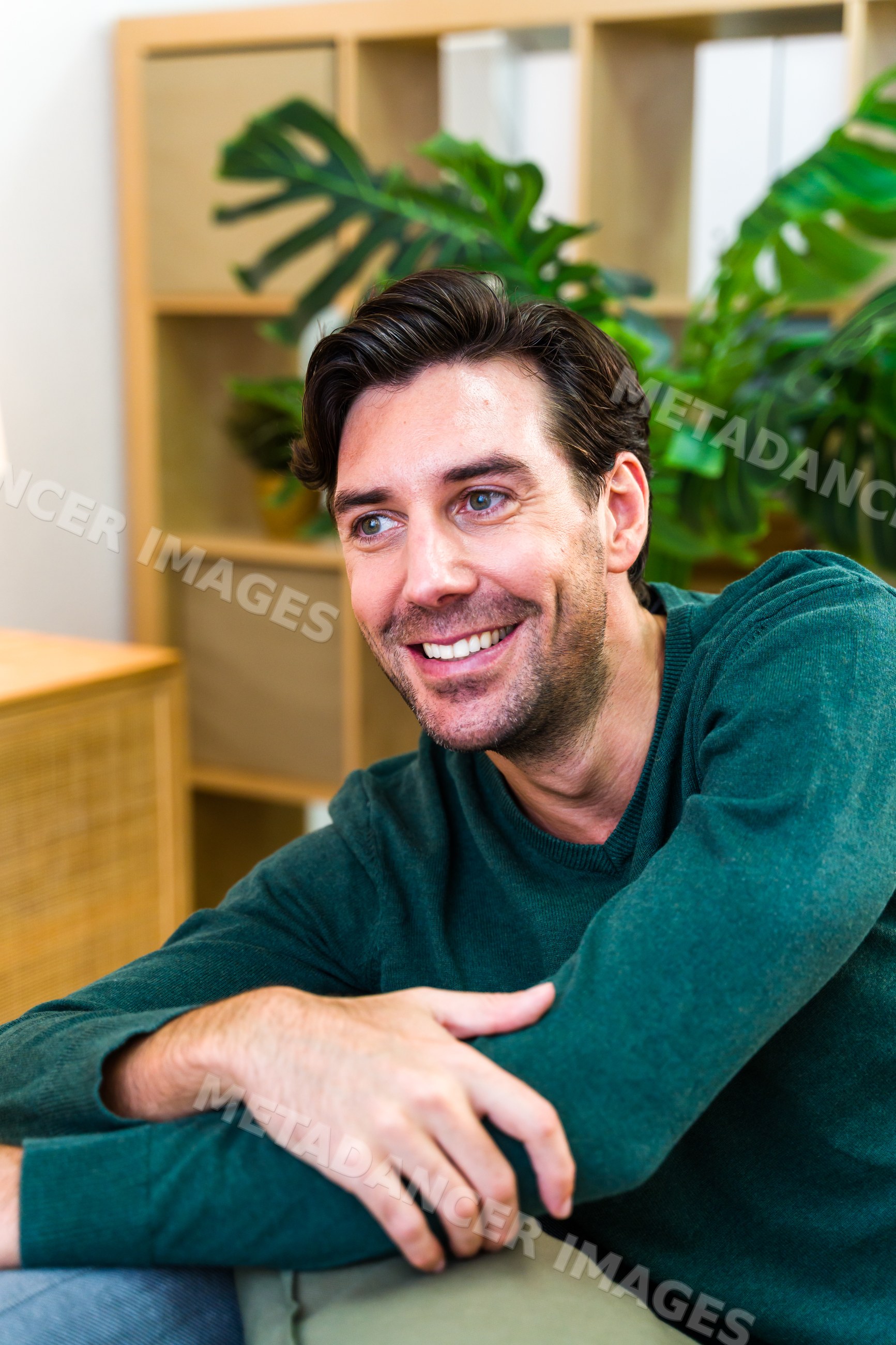 White man smiling indoors near plant and modern furniture