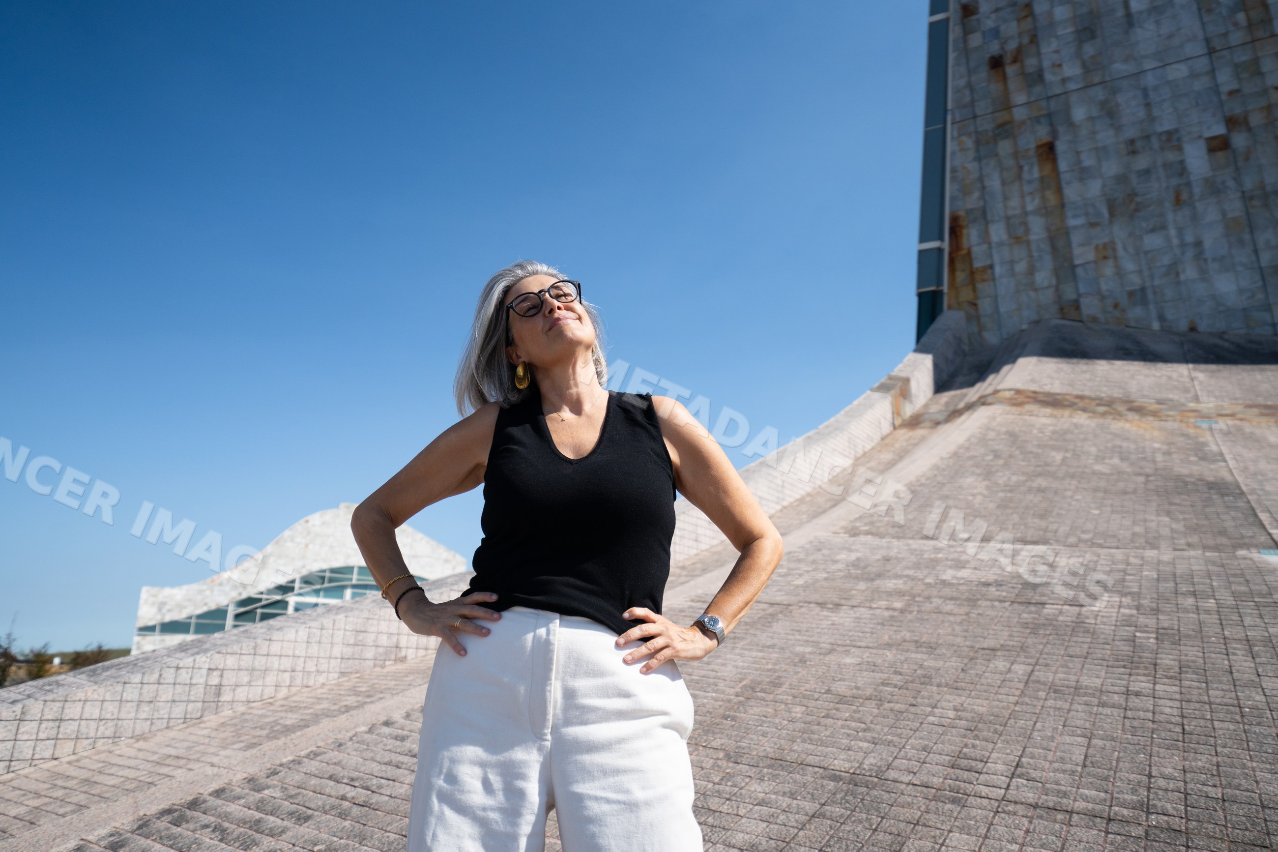 White woman posing confidently beside modern concrete architecture