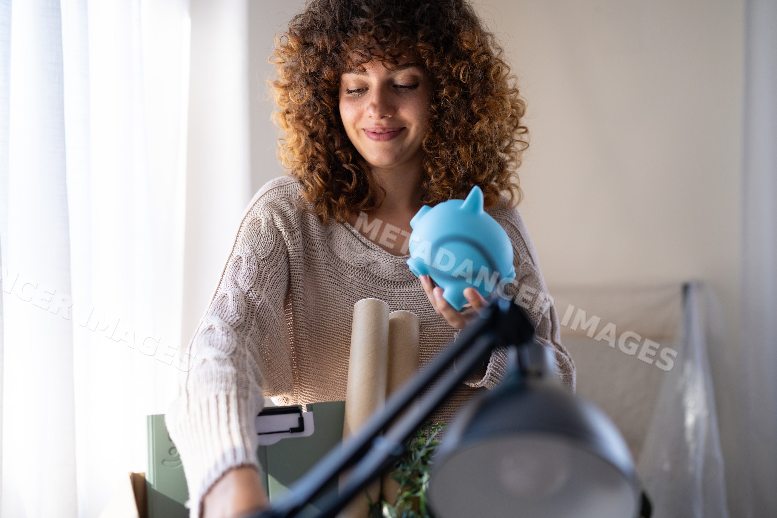 White woman organizing desk holding blue piggy bank indoors