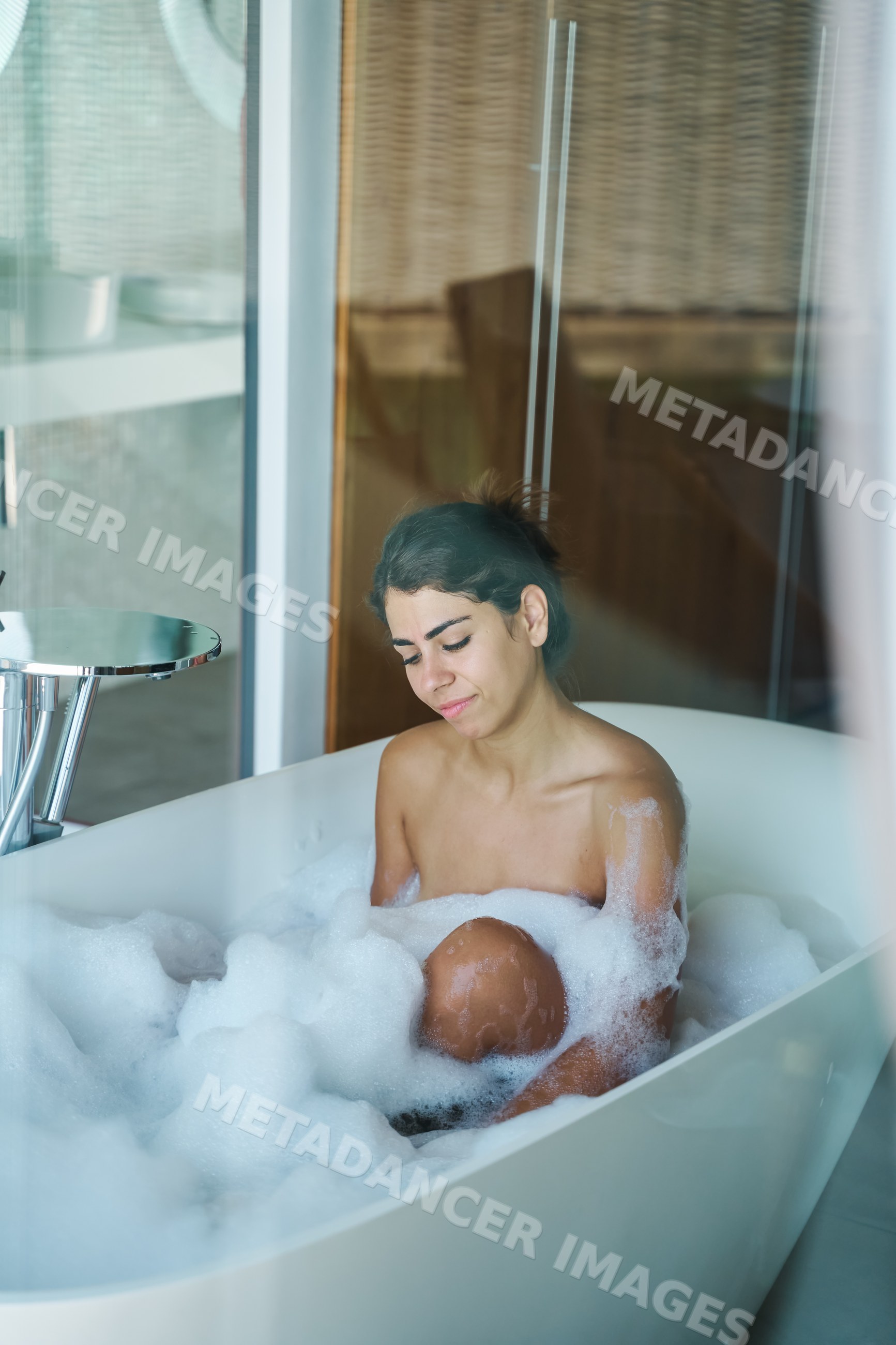 A white woman relaxes in a bubble bath inside a modern bathroom
