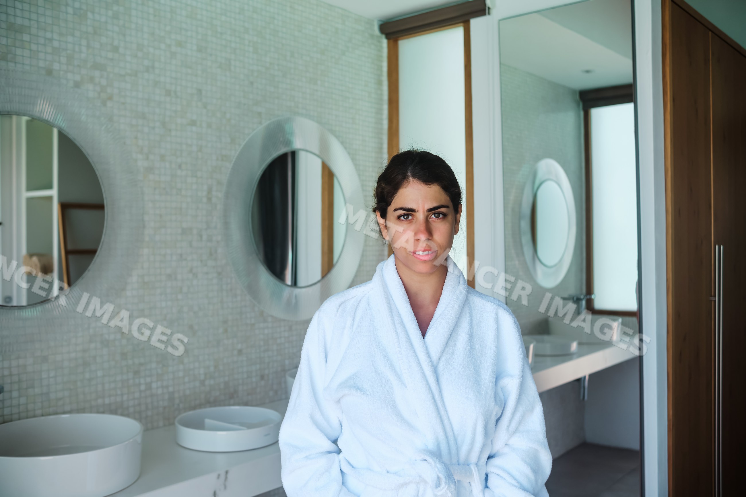 A woman wearing a white bathrobe stands in a modern bathroom