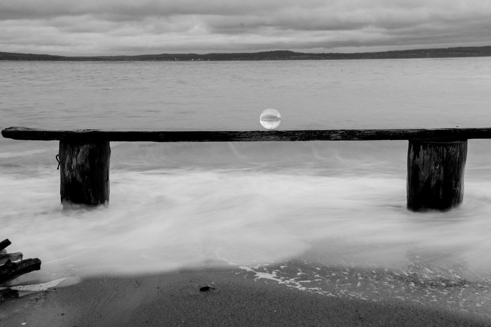 Glass sphere on wooden bench at beach with ocean waves and cloudy sky