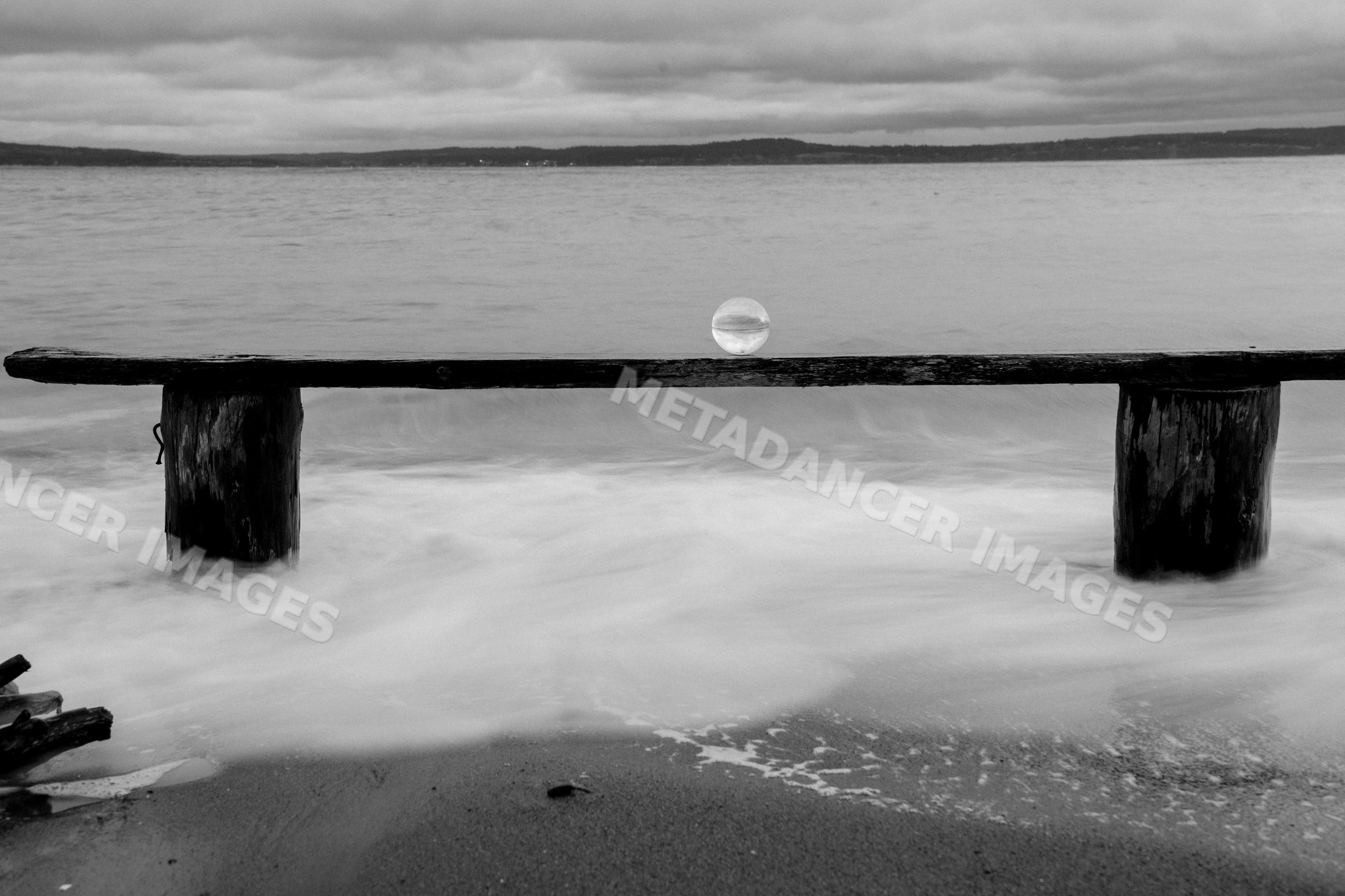 Glass sphere on wooden bench at beach with ocean waves and cloudy sky