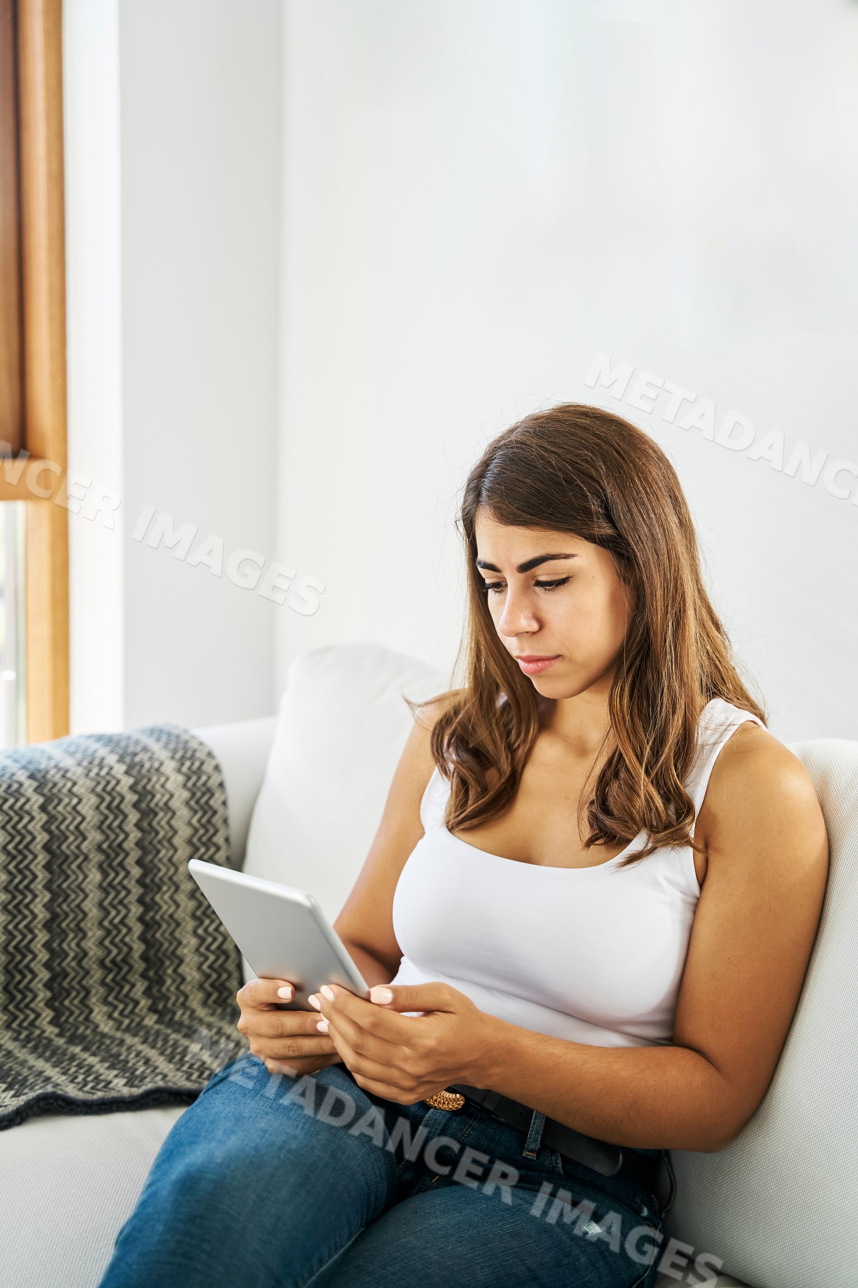 A white woman uses a tablet while relaxing on a couch indoors