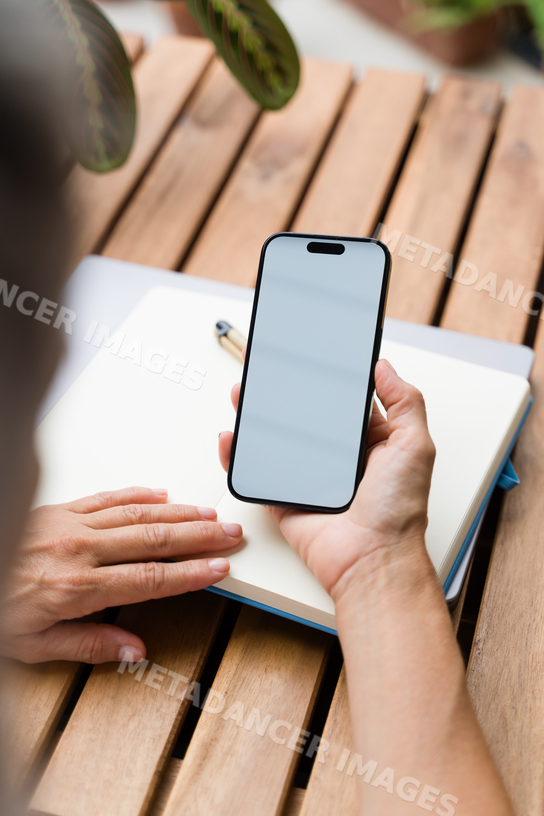 White Person holding smartphone over notebook on wooden table