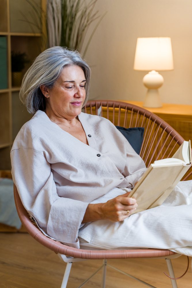 Middle-aged white woman reading book indoors in modern chair