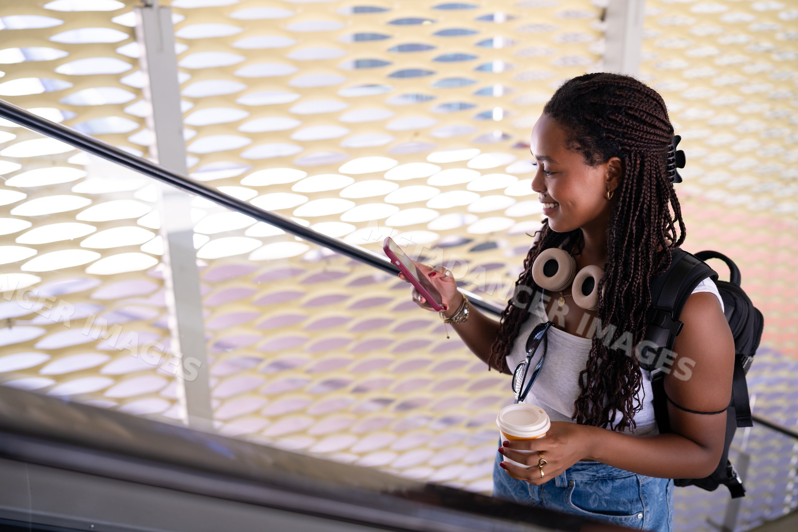 Young African American woman using smartphone and holding coffee