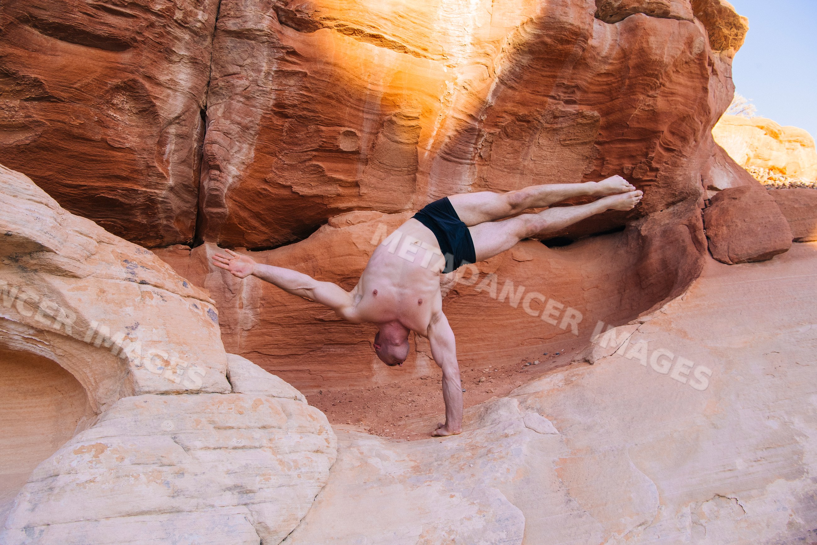 White man performing a handstand yoga pose on red rock formations