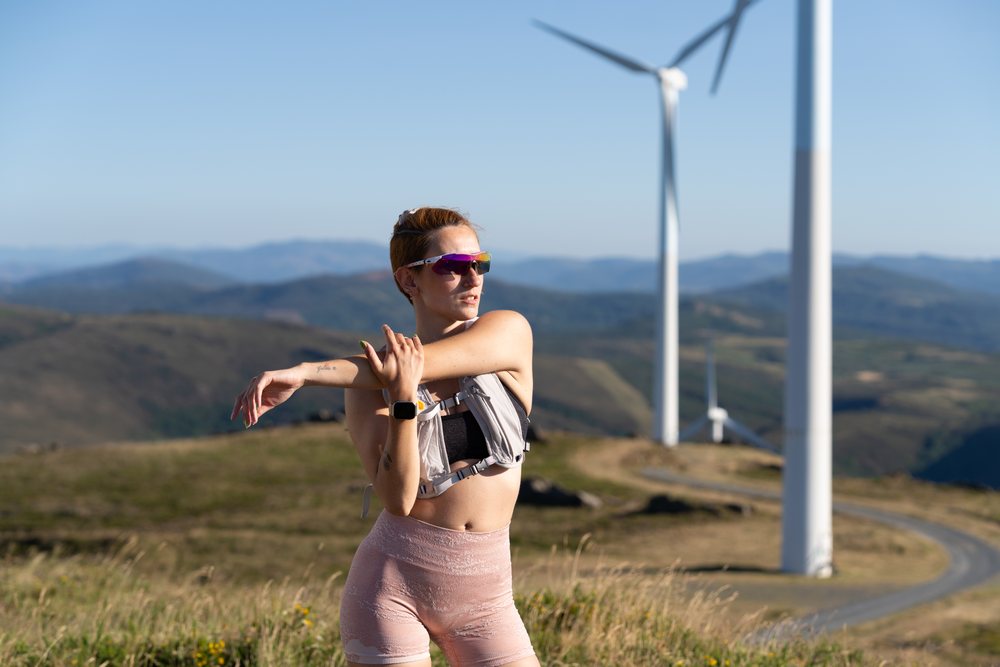 A white woman stretches during an outdoor workout near wind turbines