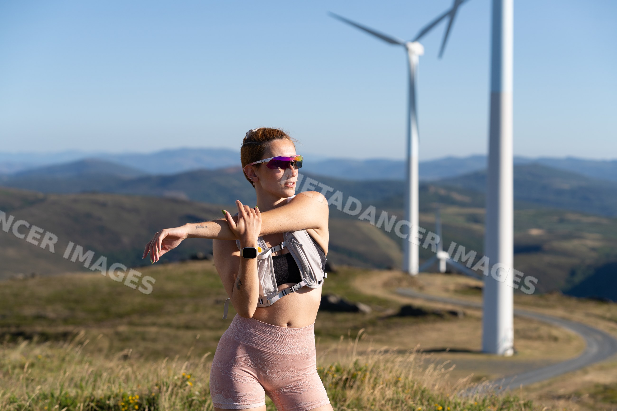 A white woman stretches during an outdoor workout near wind turbines