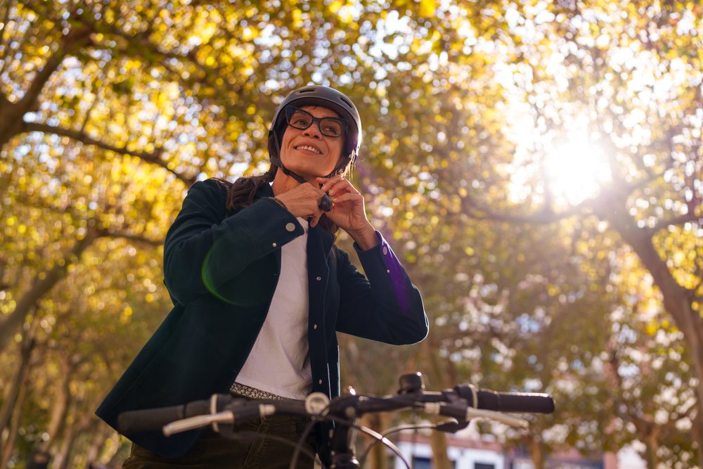 Hispanic woman fastening helmet strap on bicycle in autumn park