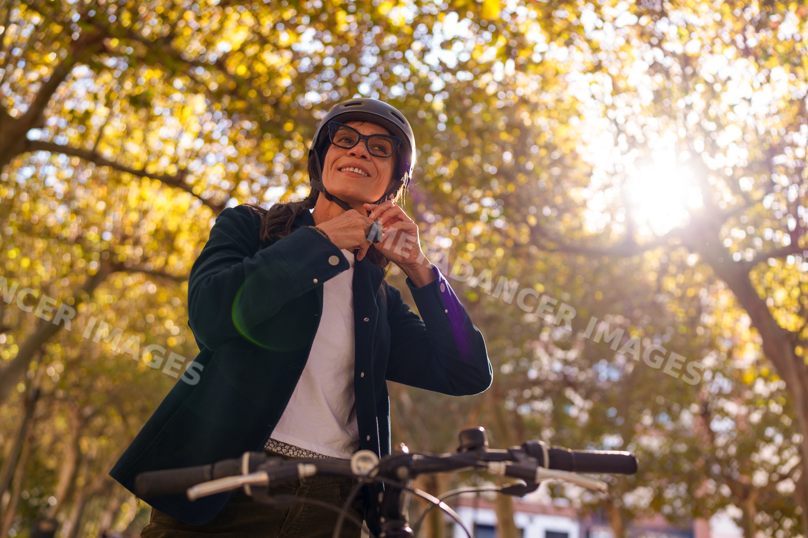 Hispanic woman fastening helmet strap on bicycle in autumn park