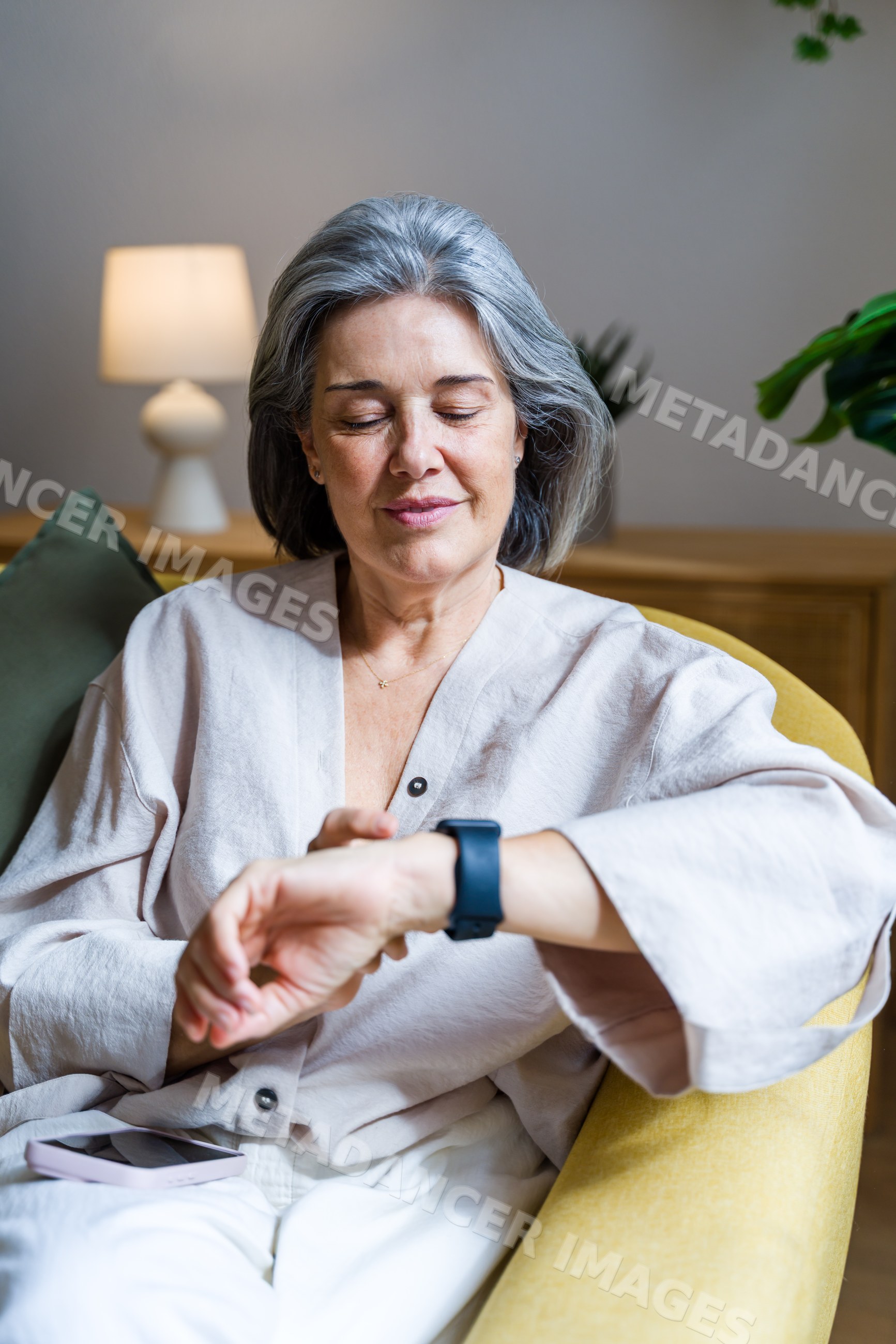 White woman checking smartwatch while seated indoors on yellow chair