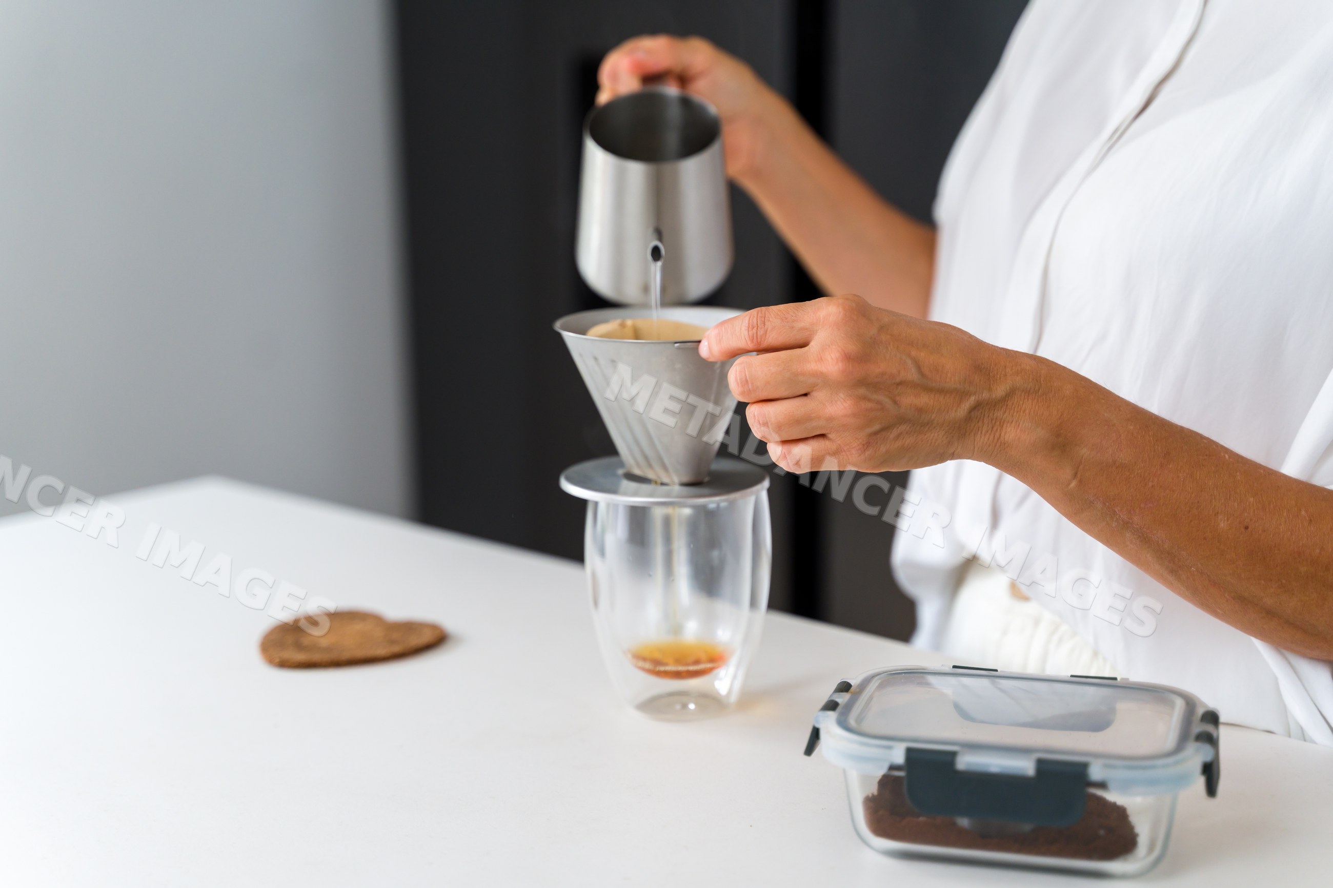 Hand brewing coffee with a metal kettle and filter in a kitchen