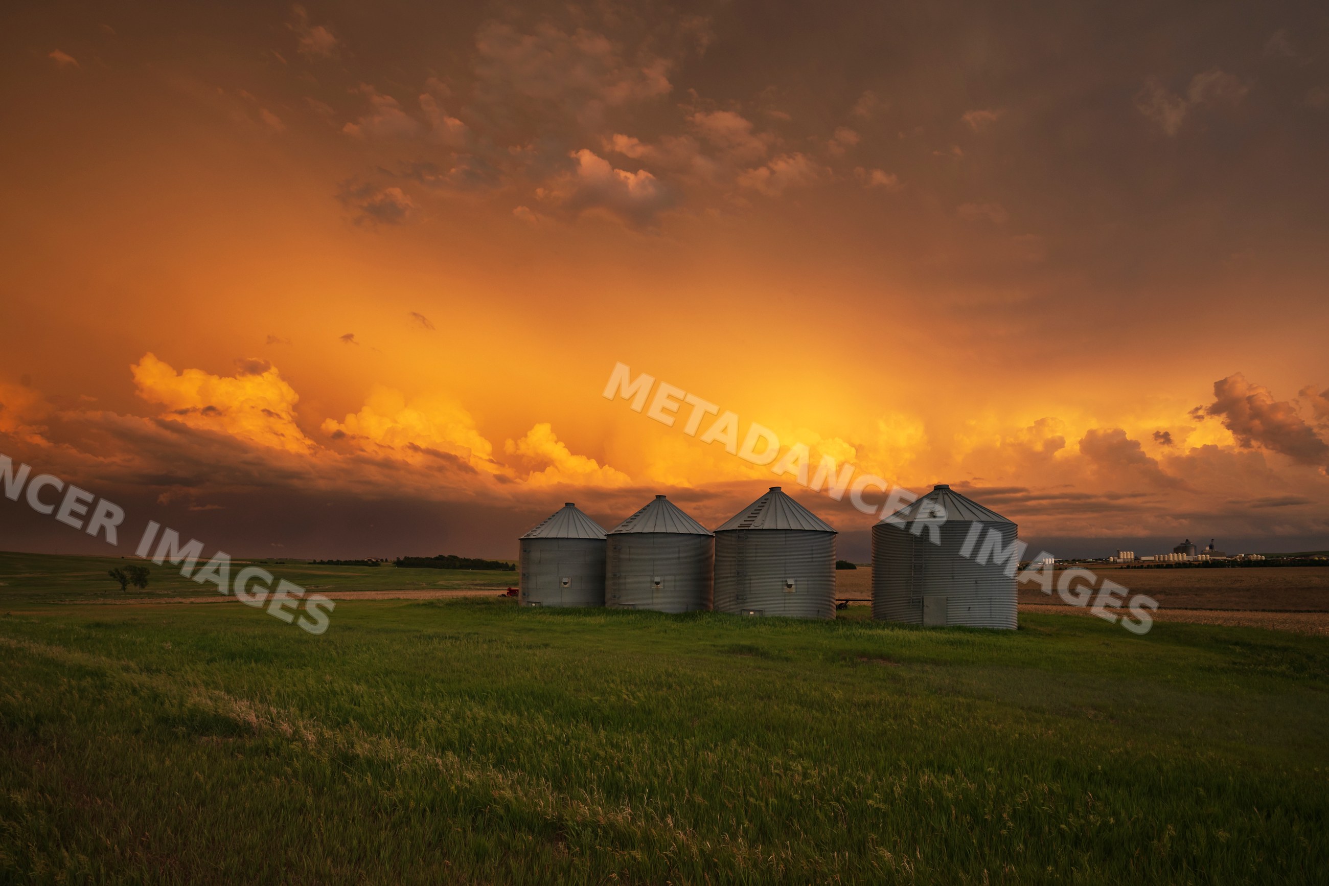 Sunset over grain silos in south dakota farm field with storm clouds