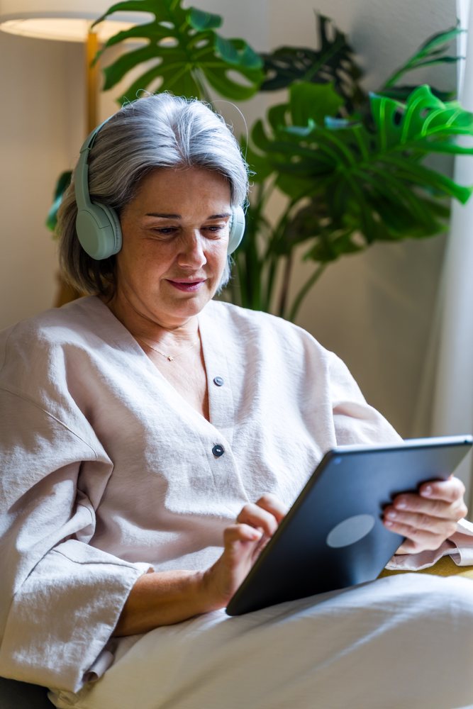 White woman using tablet indoors with headphones near indoor plant