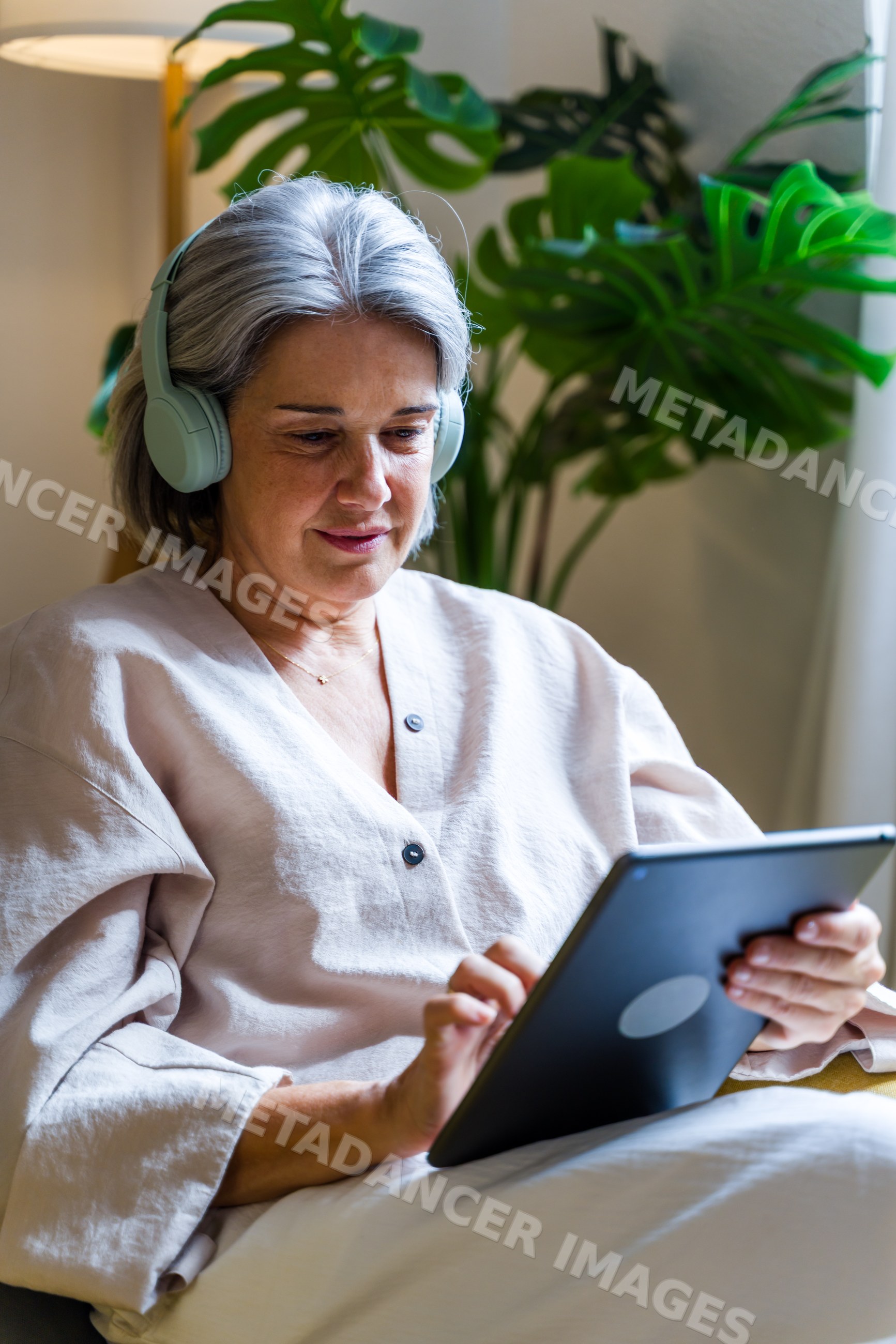 White woman using tablet indoors with headphones near indoor plant