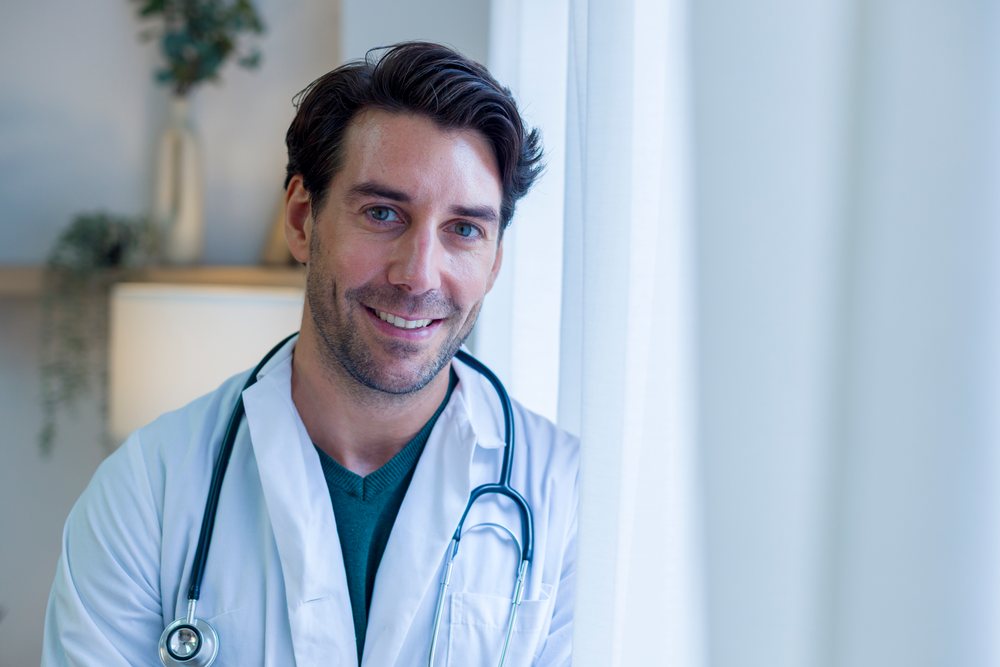 Male doctor smiling indoors with stethoscope in home setting