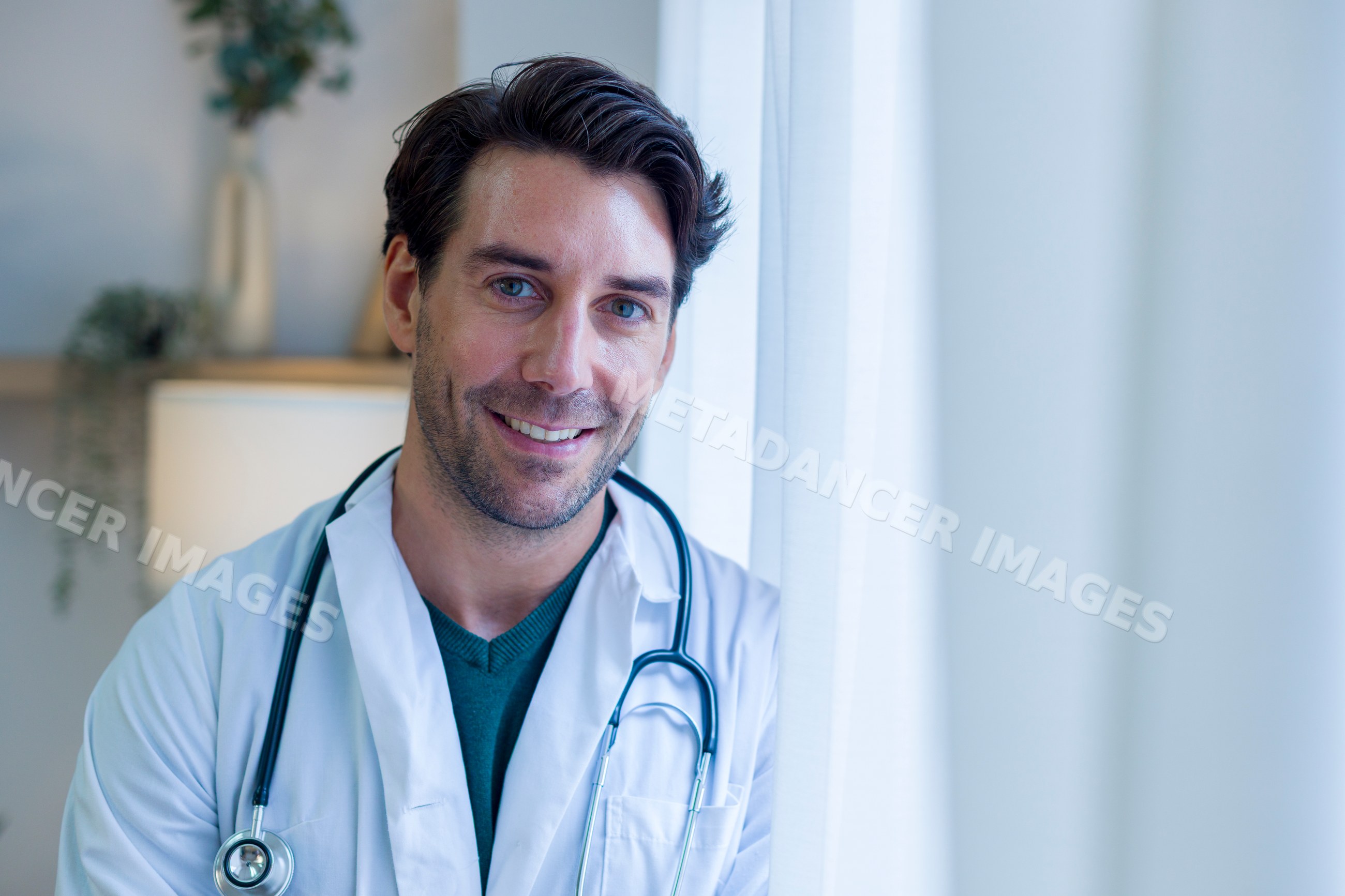 Male doctor smiling indoors with stethoscope in home setting