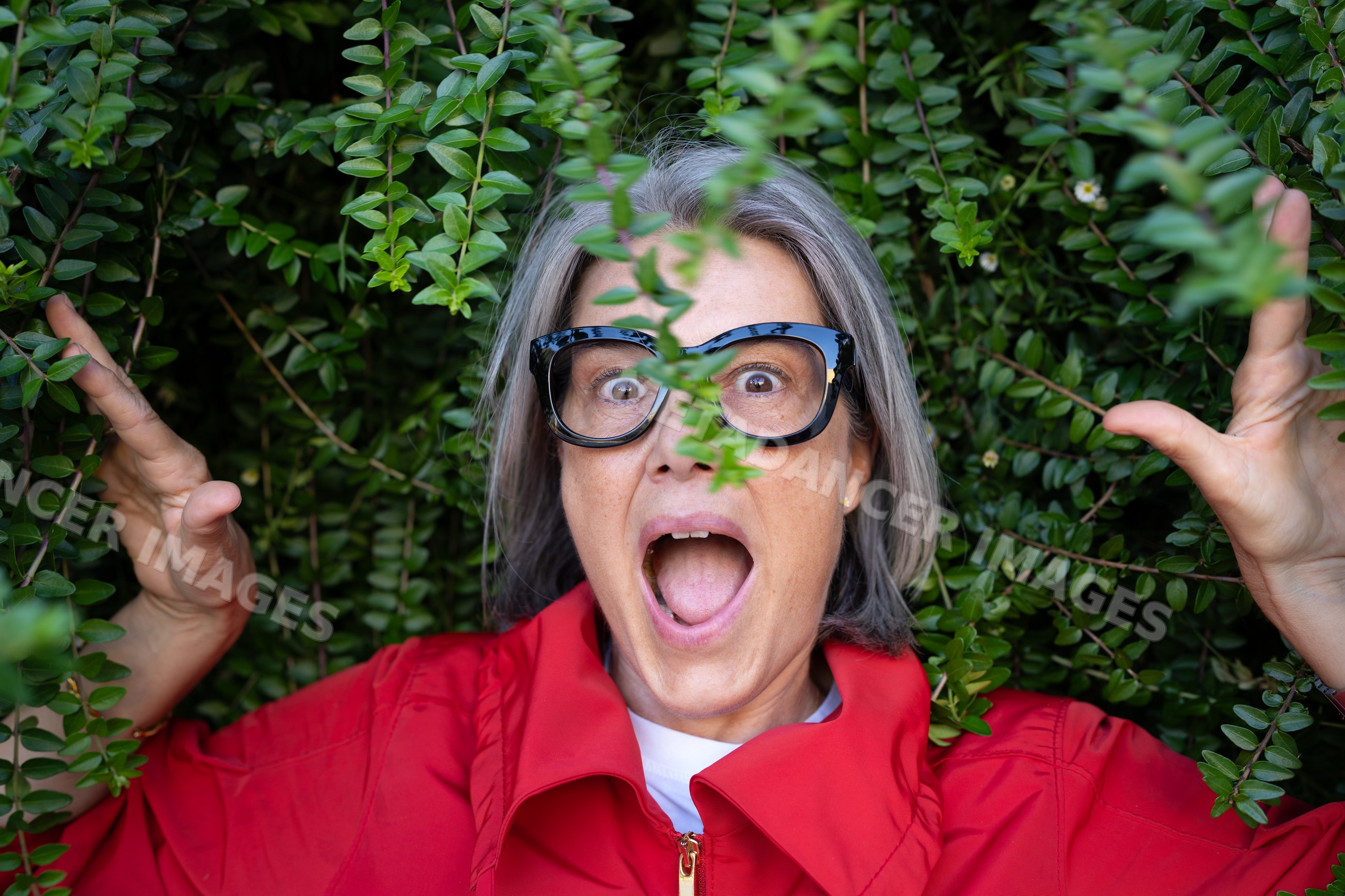 White woman with glasses expressing surprise in green foliage outdoors