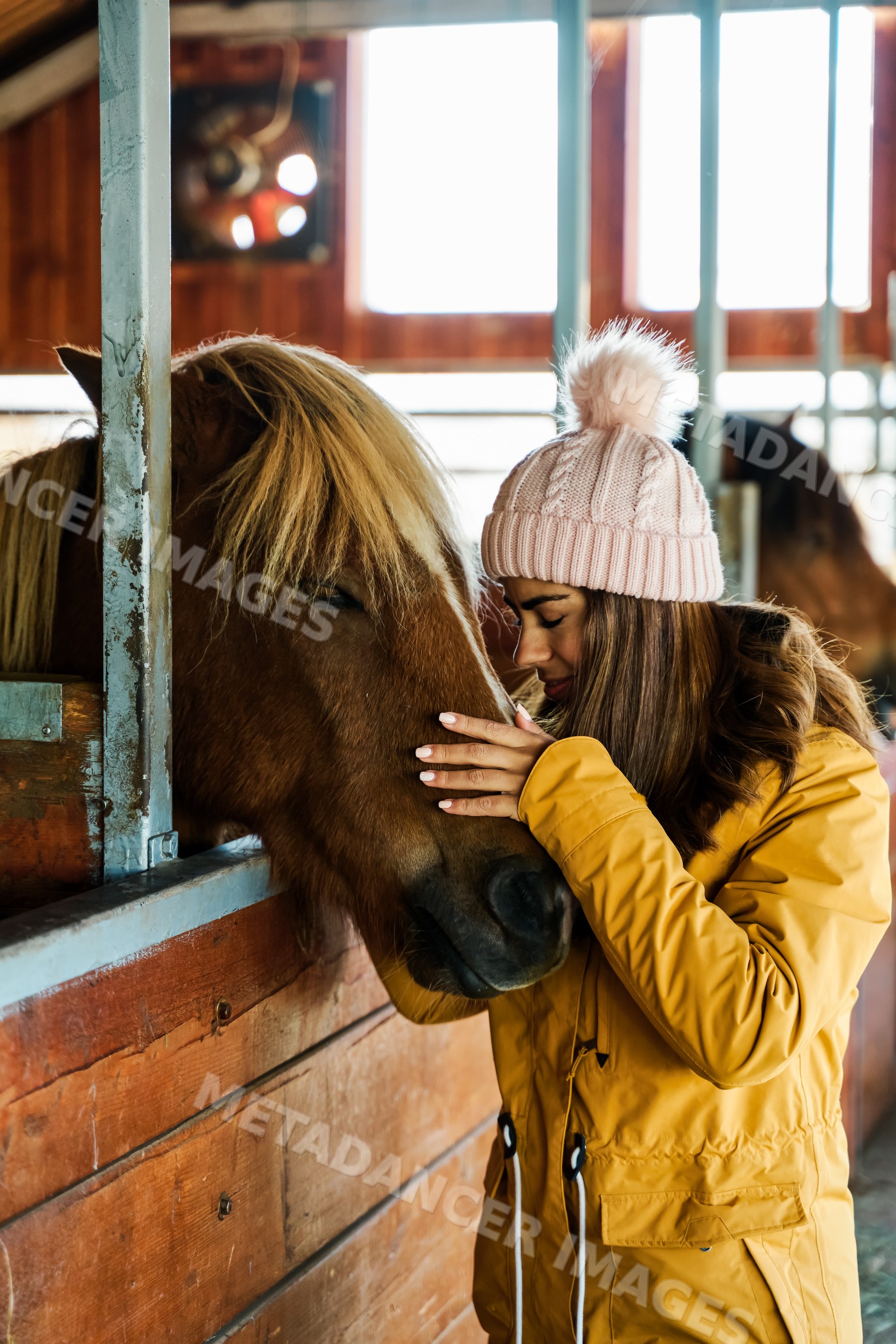 A white woman gently pets a horse inside a stable in Iceland