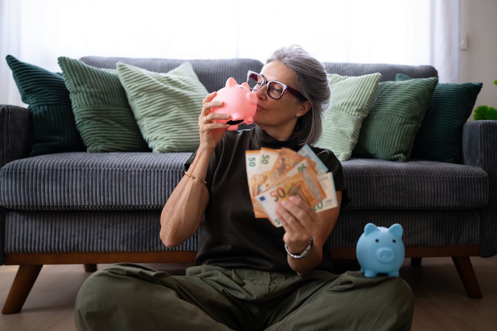 White woman holding piggy banks and euro banknotes sitting on floor