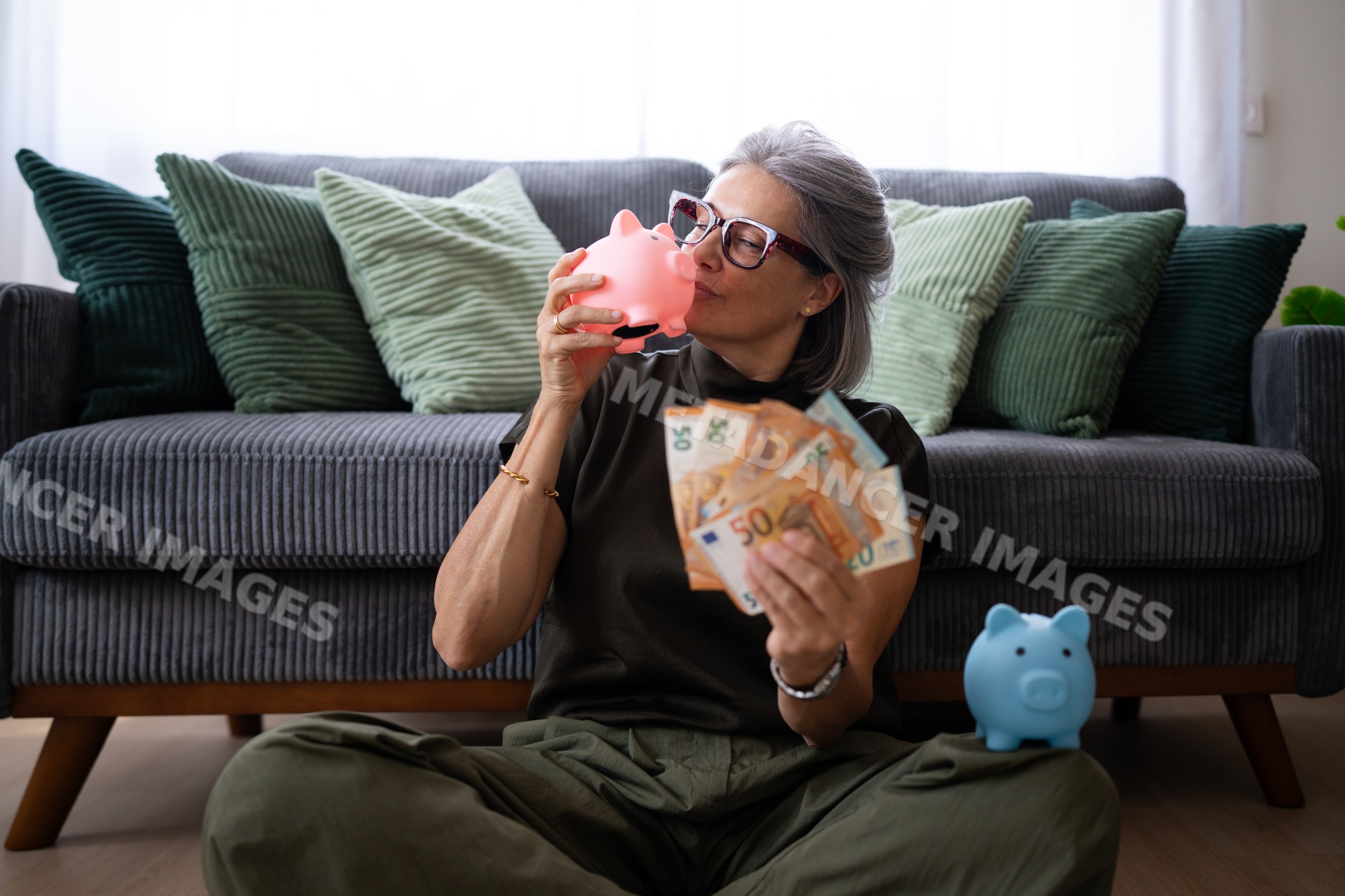 White woman holding piggy banks and euro banknotes sitting on floor
