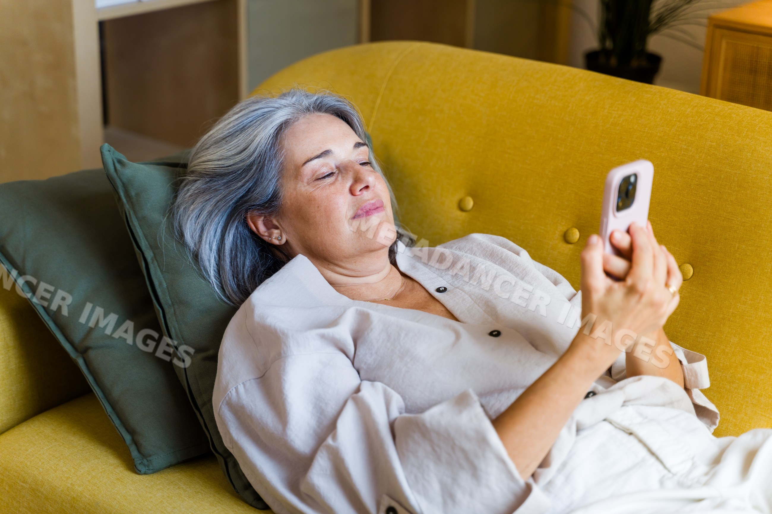 Middle-aged white woman relaxing on sofa using smartphone