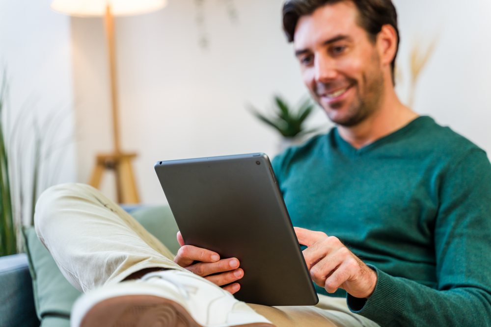White man using tablet on couch in living room