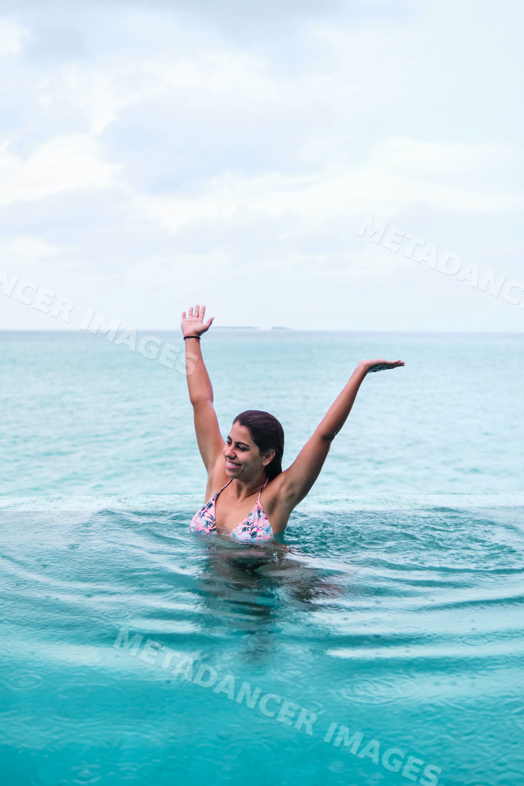 A white woman raises her arms swimming in an infinity pool