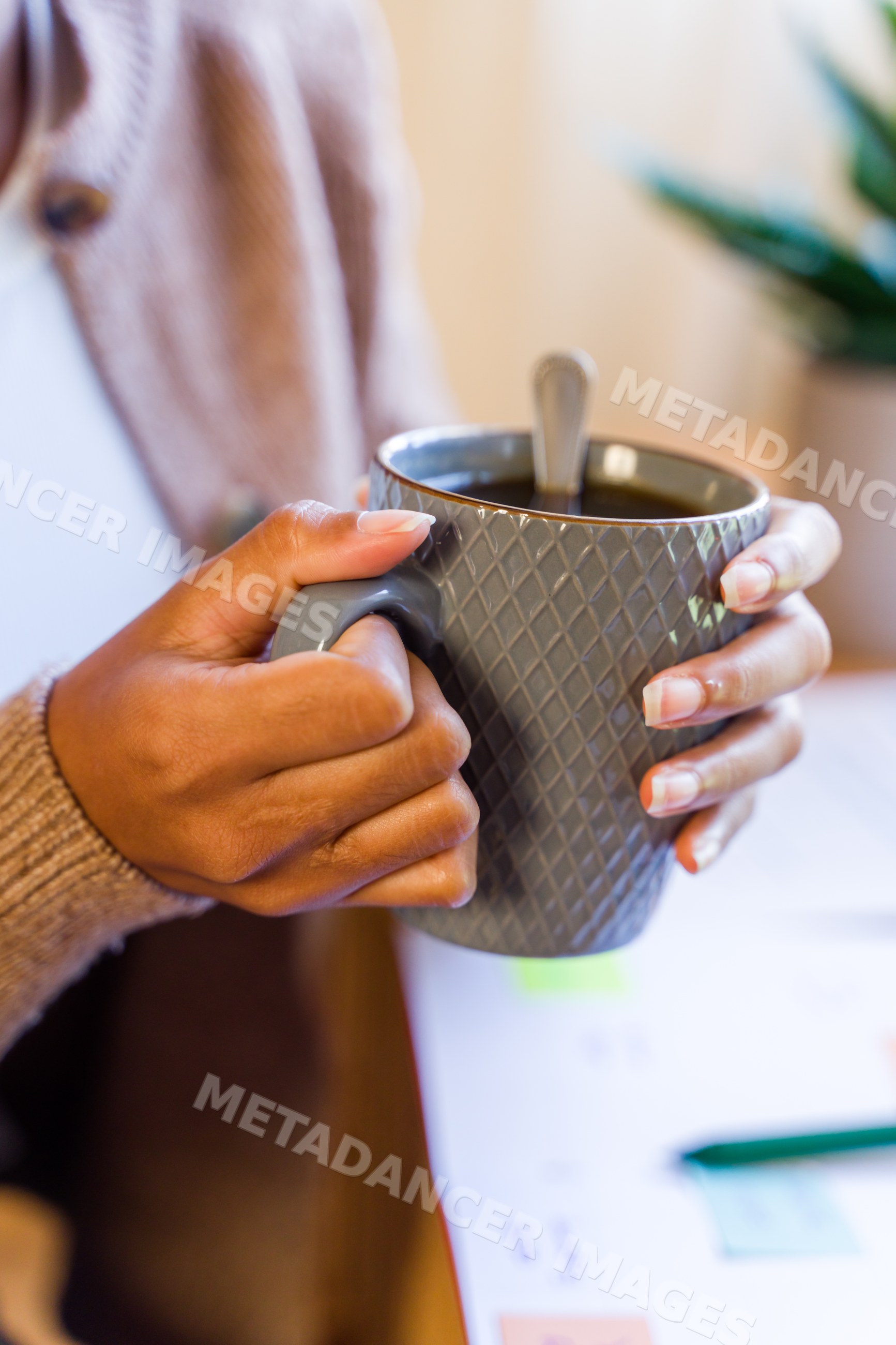 Hands holding gray textured coffee mug indoors by table with papers