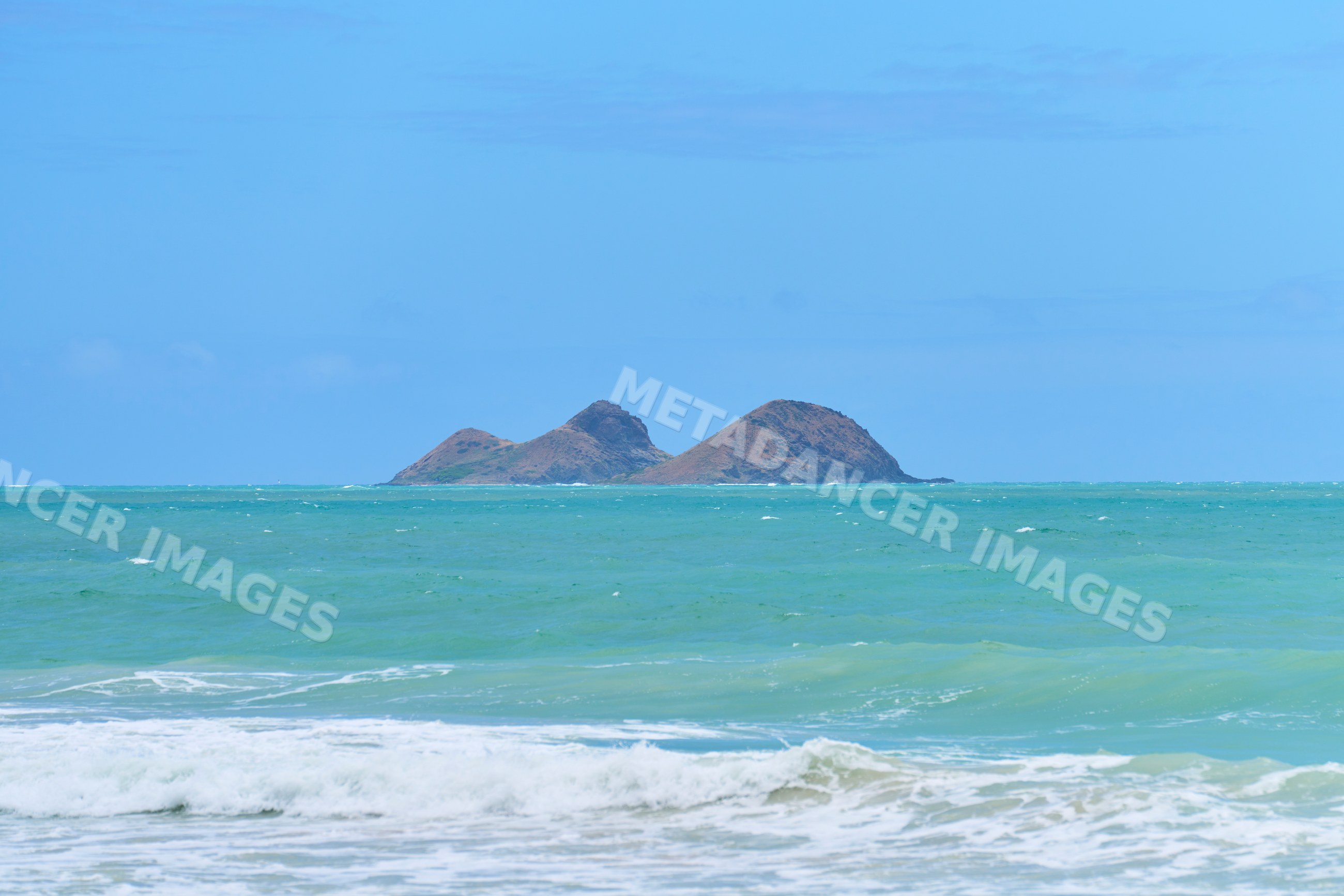 Island in the ocean with waves under blue sky