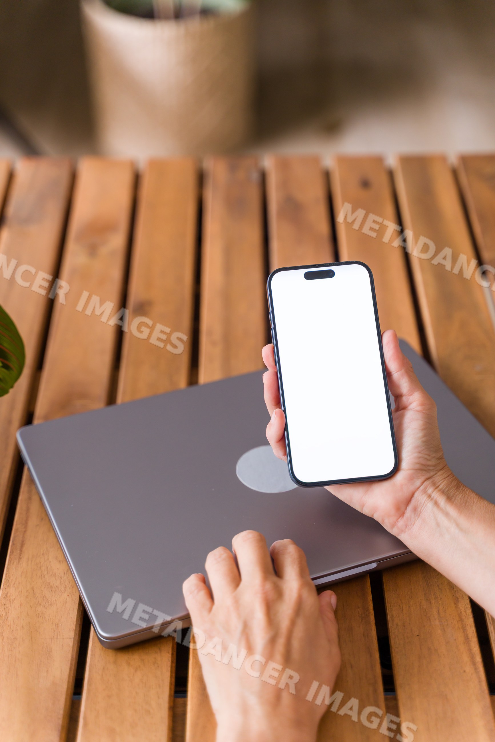 Hand holding smartphone with blank screen above closed laptop
