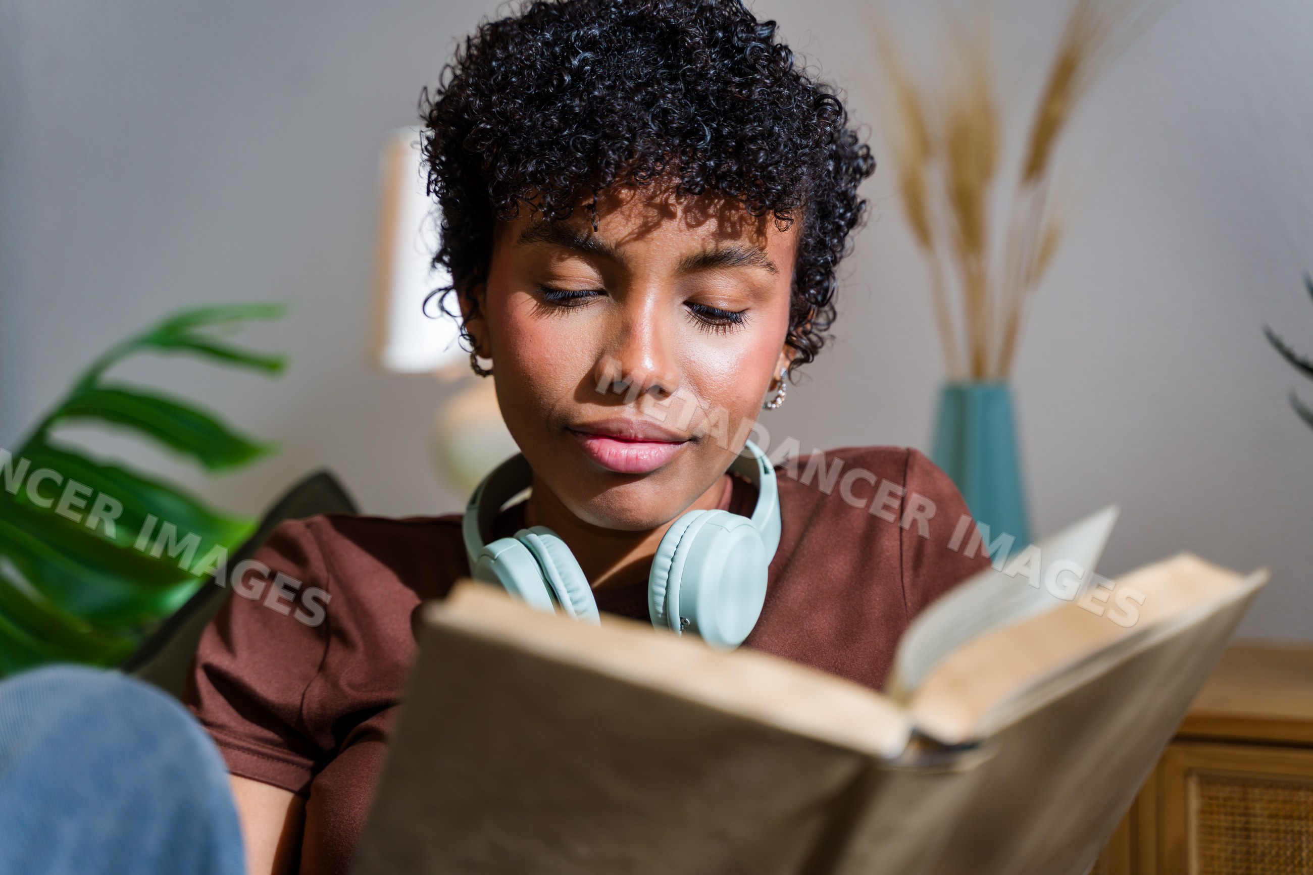 African American woman reading a book indoors wearing headphones