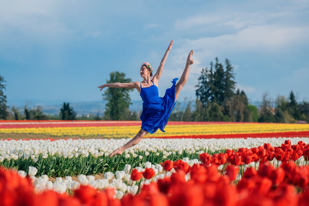 Ballet white dancer leaping through colorful tulip field outdoors