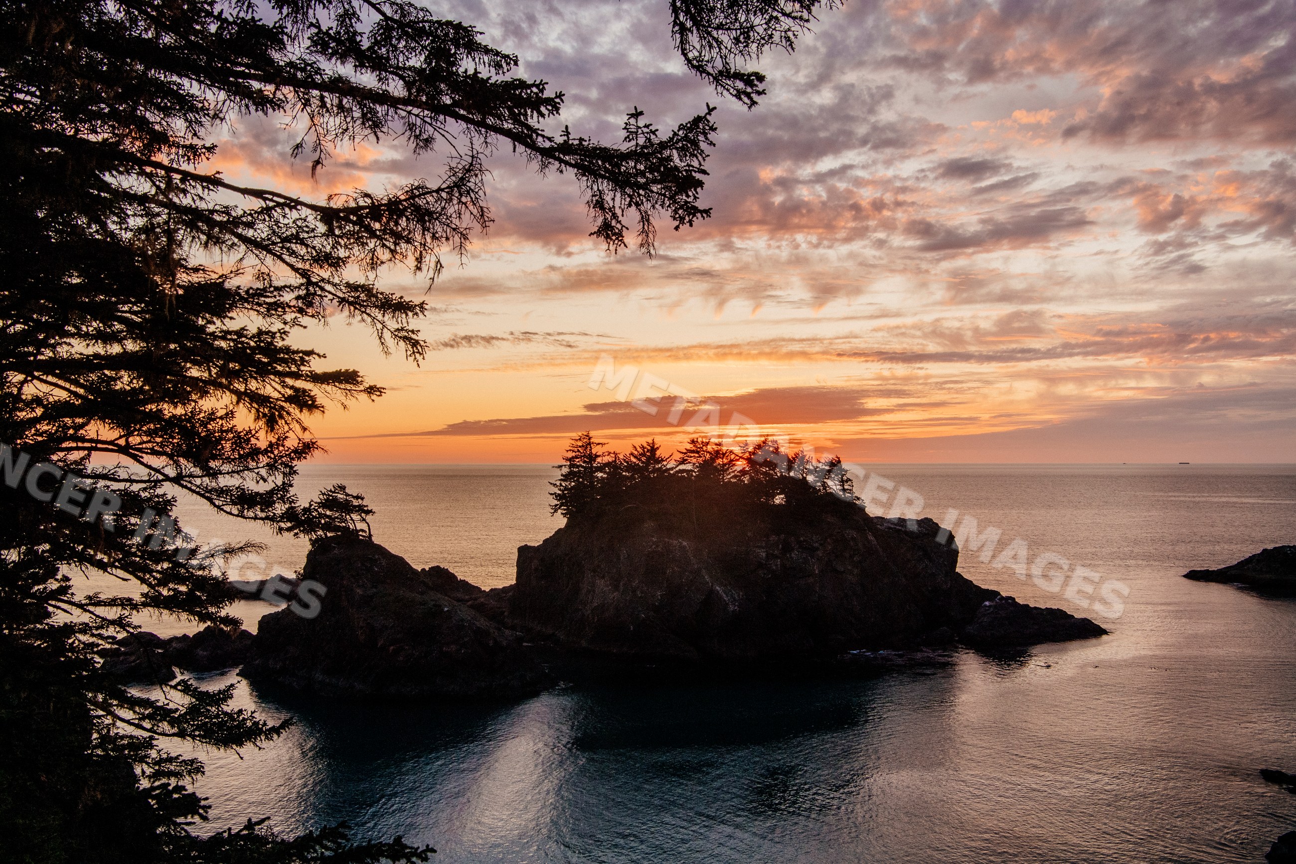 Sunset over rocky island with trees in ocean Oregon